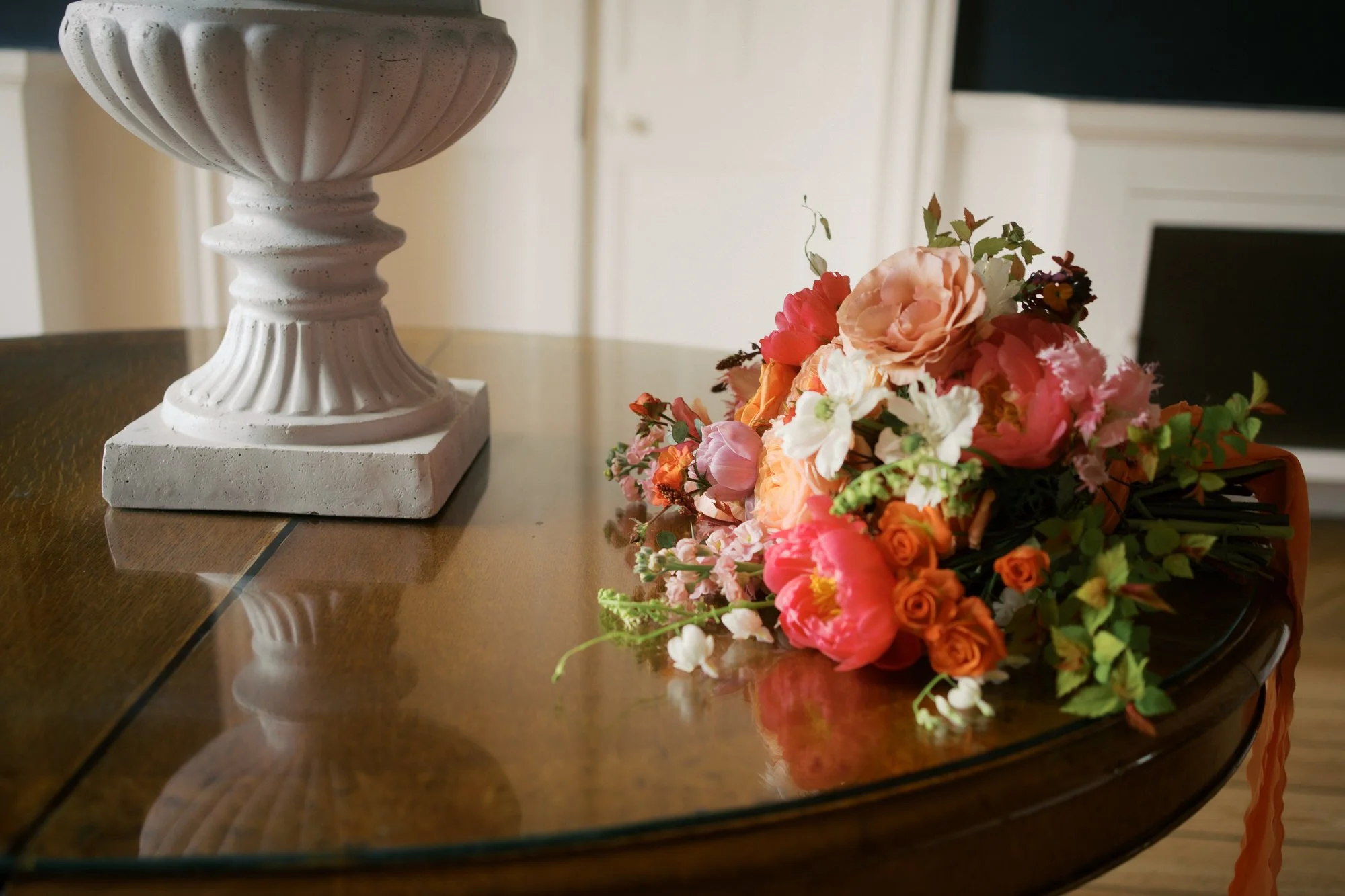  A coral and peach bridal bouquet on a polished table beside a stone urn 