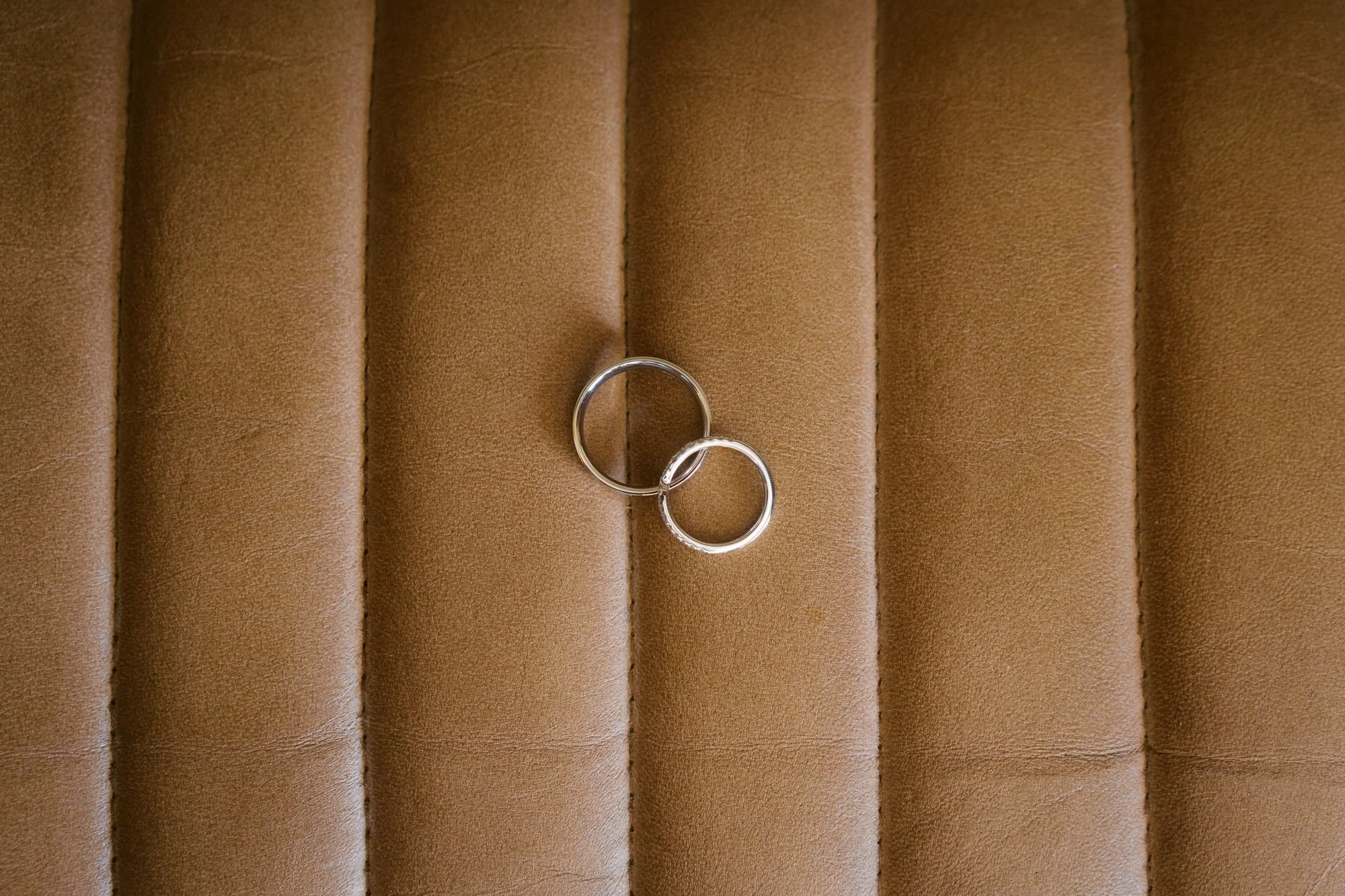  Two wedding rings resting on tan leather upholstery 
