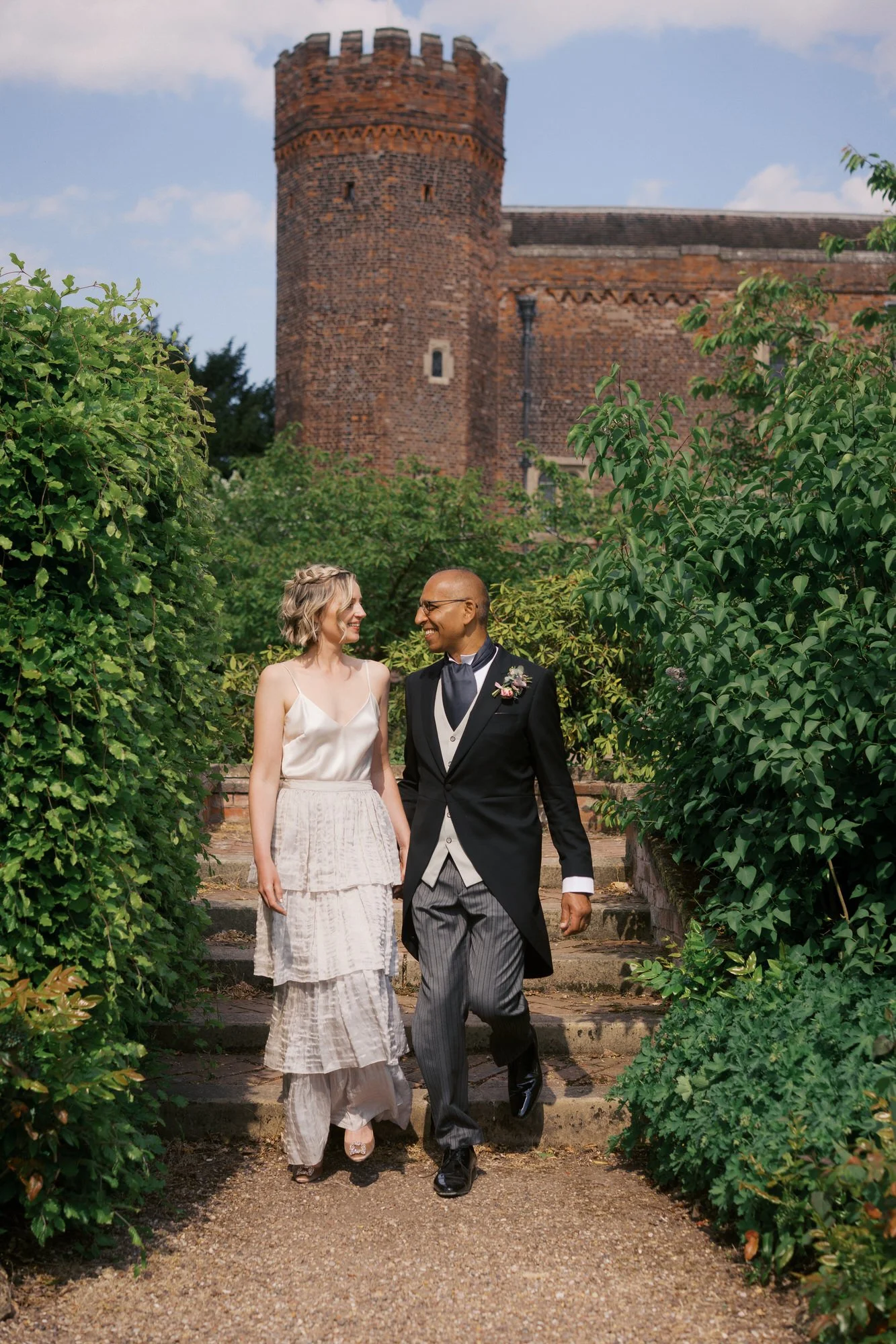  A couple walking down garden steps between hedges with the Hodsock Priory tower behind 