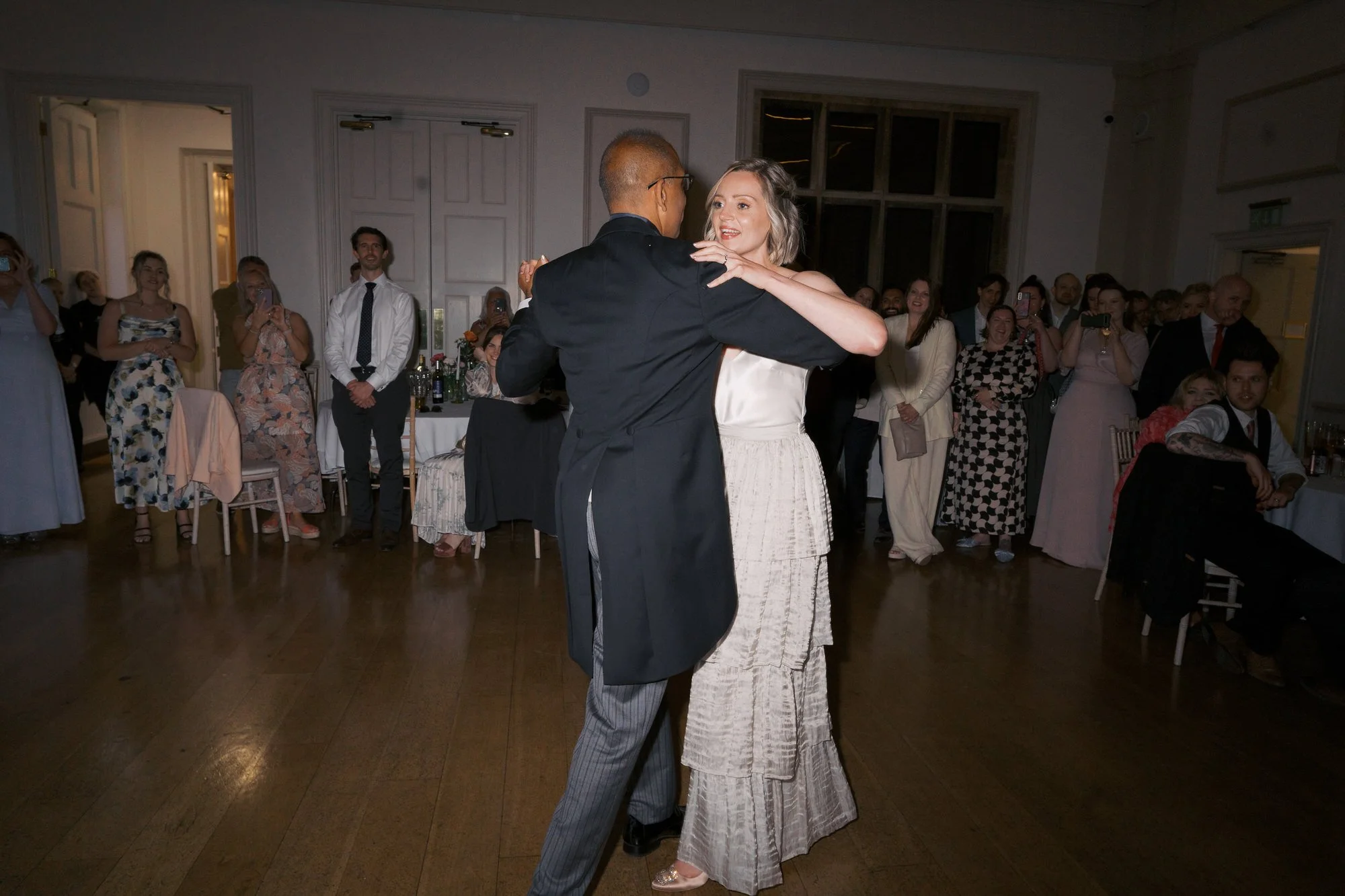  A couple dancing their first dance in the ballroom at Hodsock Priory as guests look on 