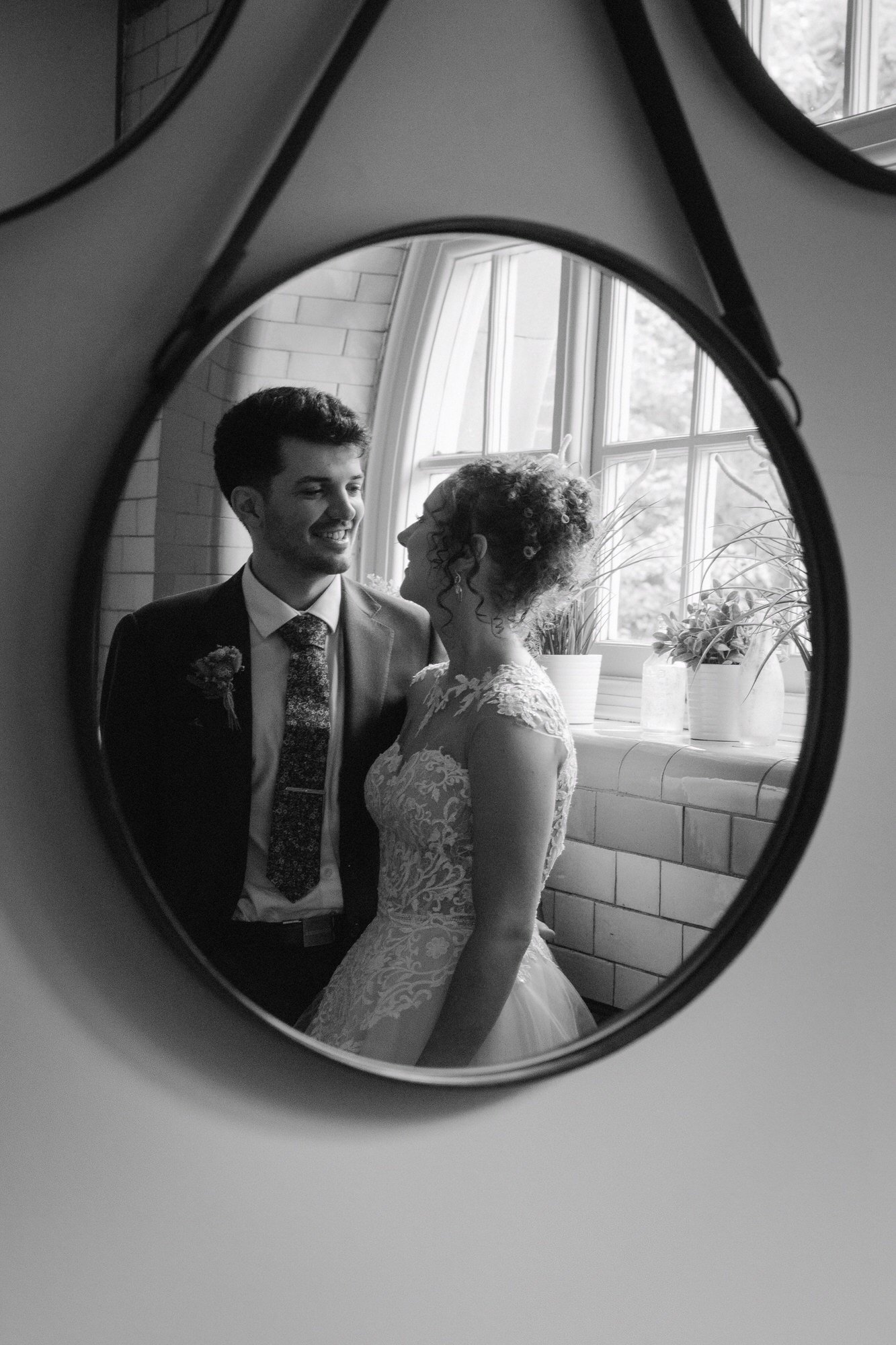  Black and white reflection of a bride and groom smiling at each other in a round mirror, The Pumping House, Ollerton 