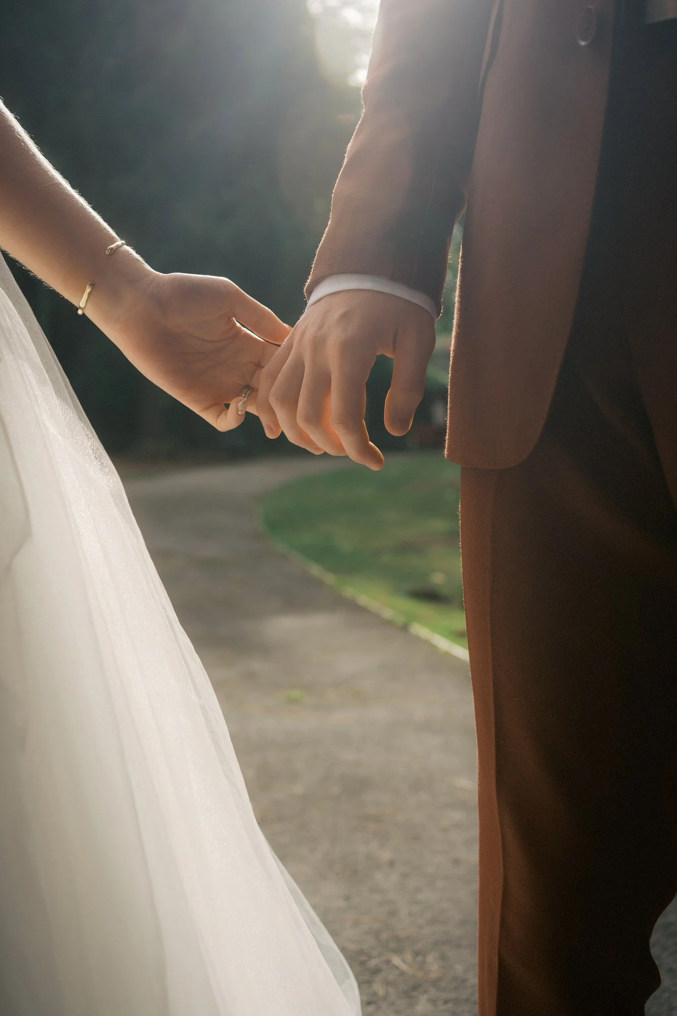  Close-up of a bride and groom holding hands on a path with sunlight behind them, The Pumping House, Ollerton 
