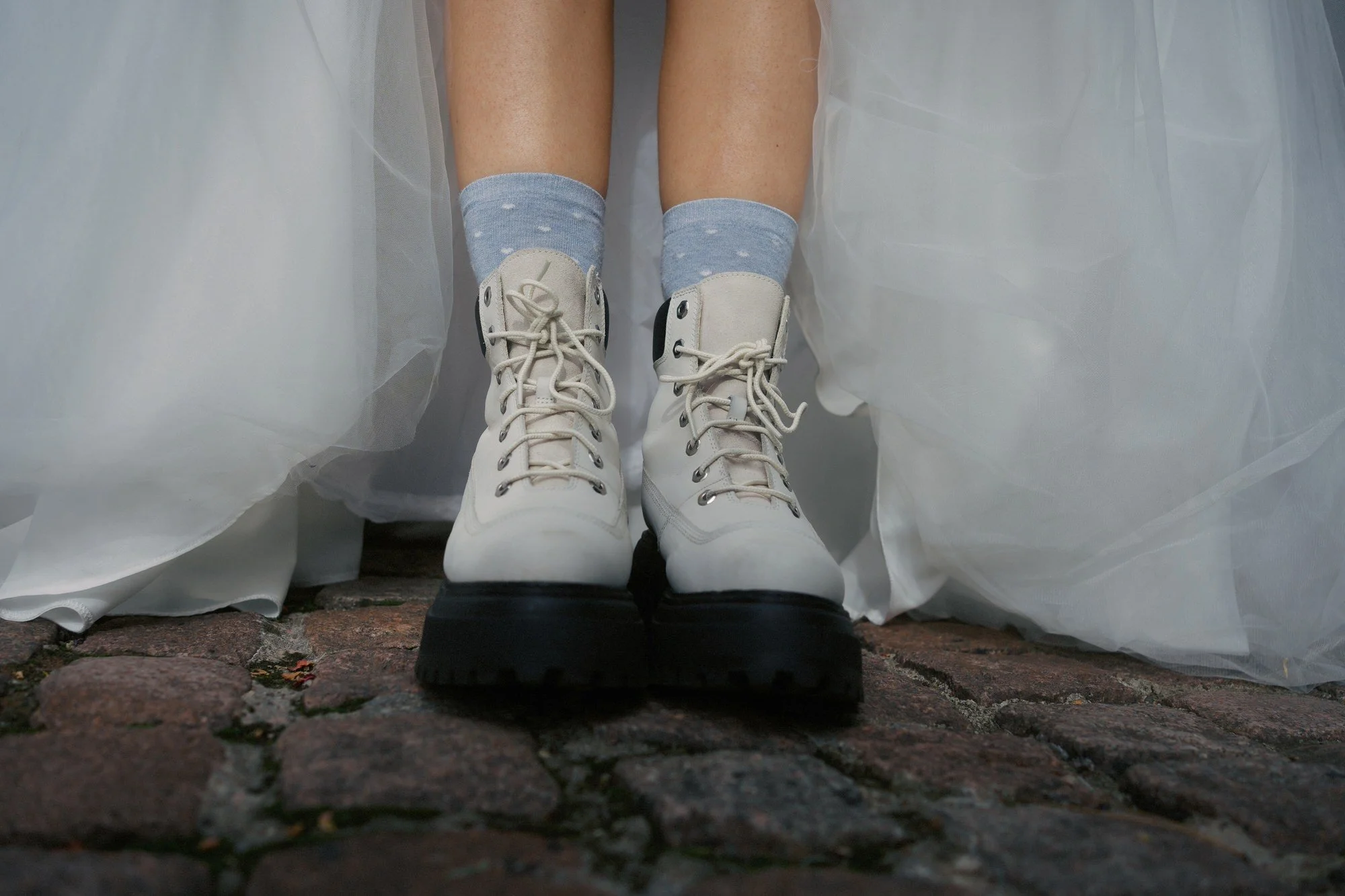  A bride's white lace-up Timberland boots and blue spotted socks beneath her dress, on cobbles with confetti petals, The Pumping House, Ollerton 