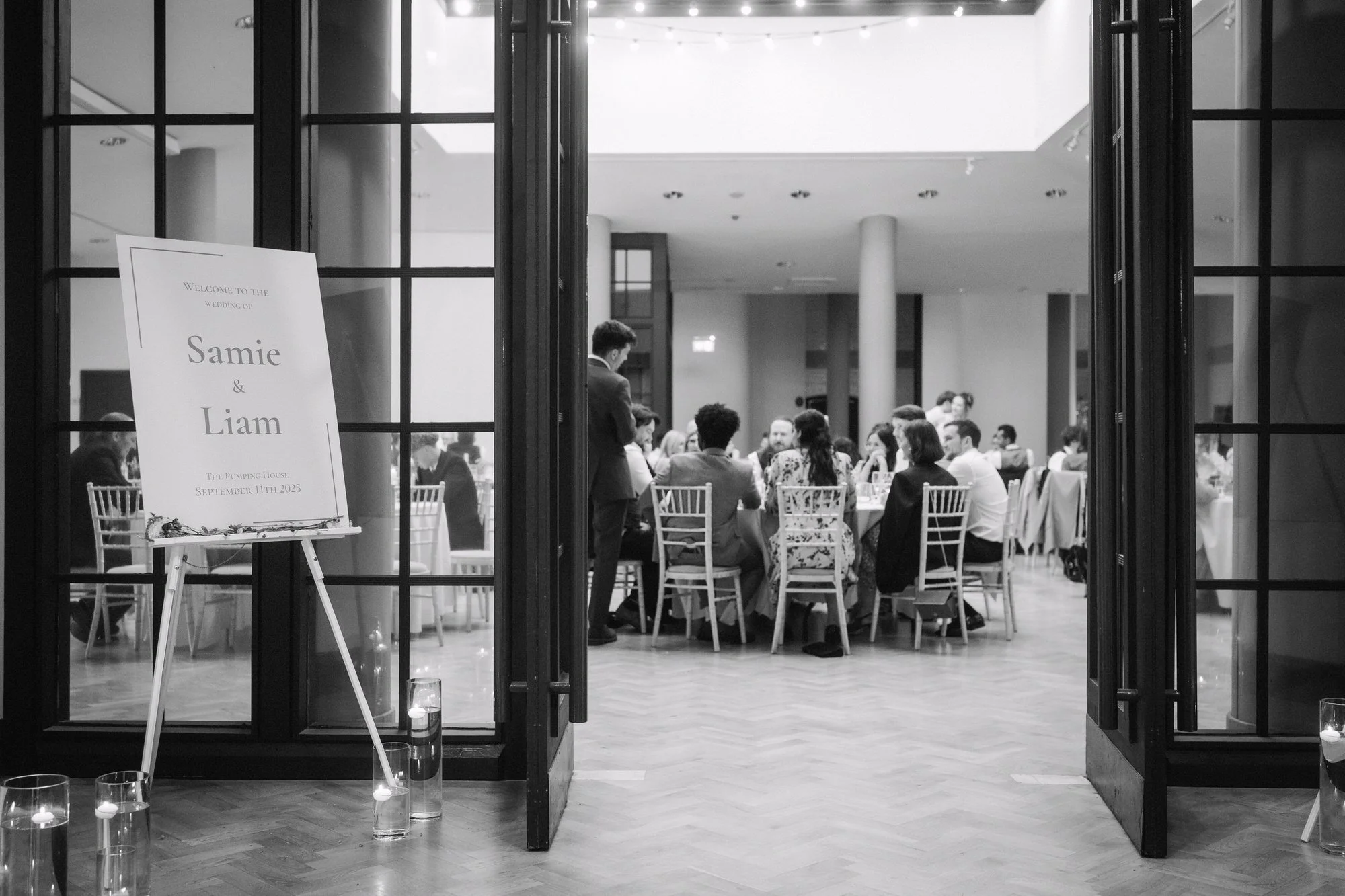  Black and white view through open glass doors into the dining hall, with guests seated, The Pumping House, Ollerton 