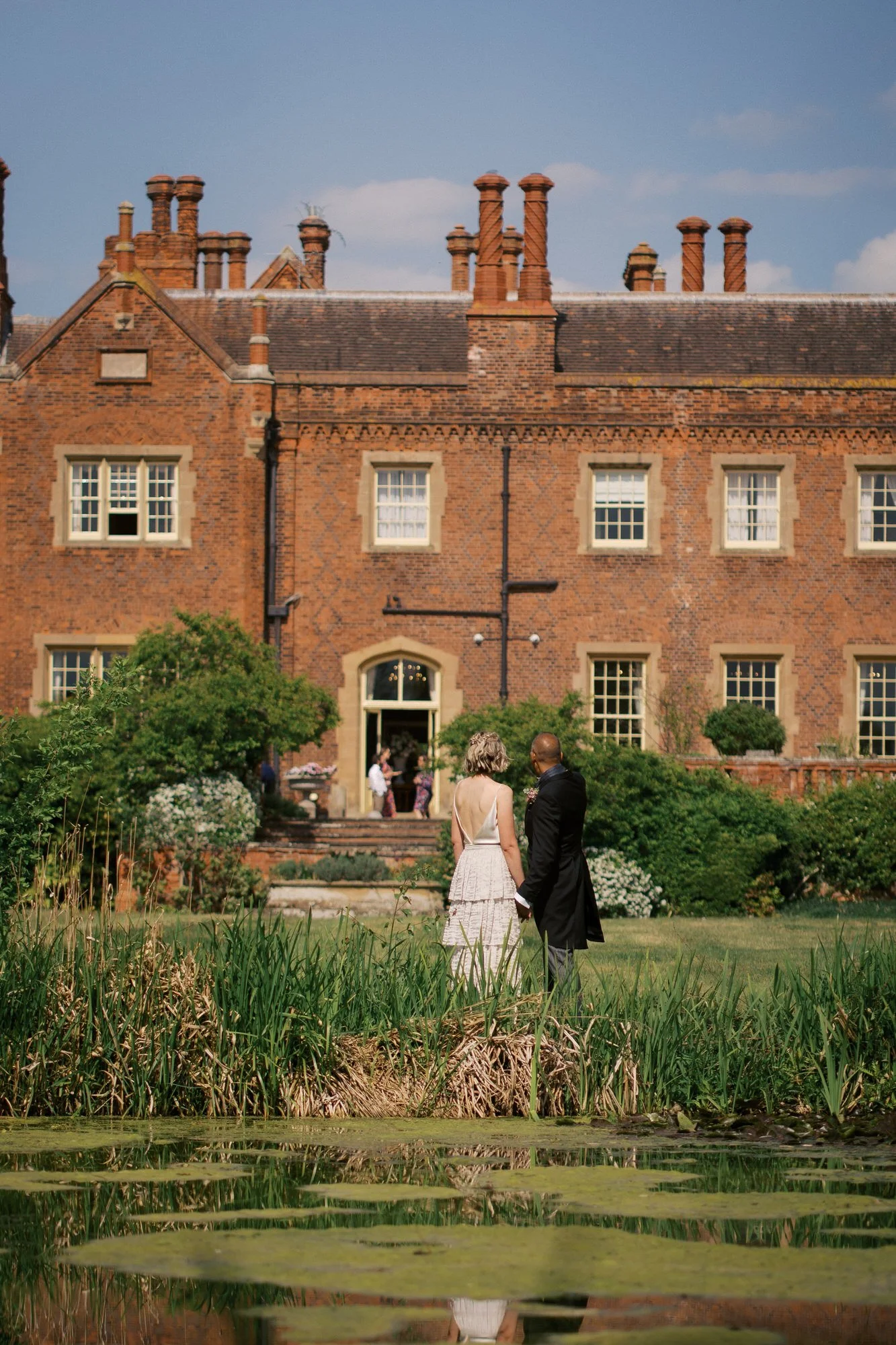 A couple standing beside a lily pond with the red-brick house behind them