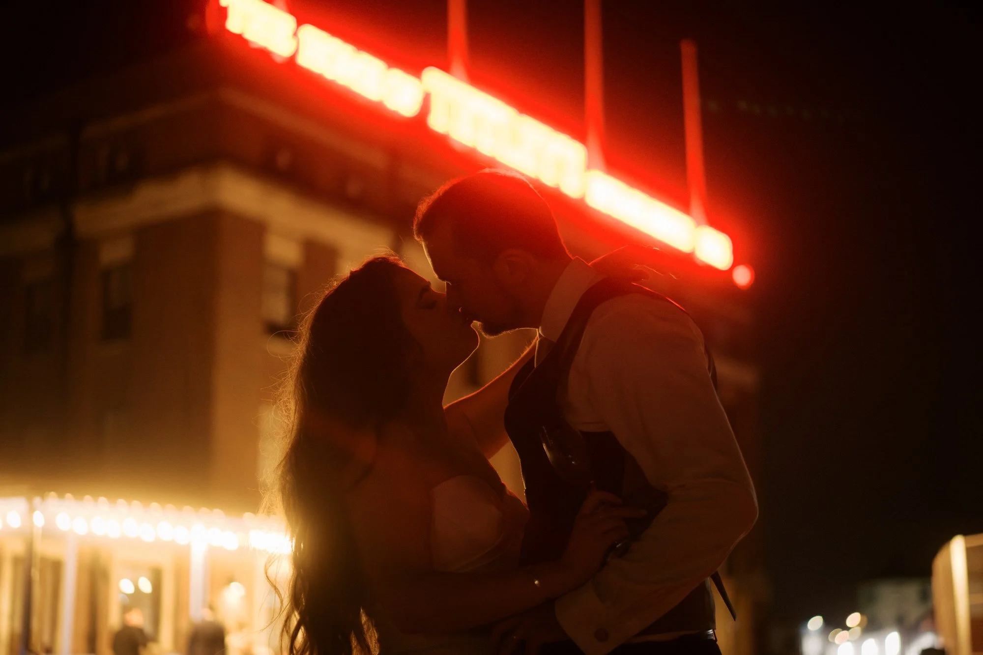 Bride and groom kissing at night beneath the red neon lettering of The Tetley in Leeds.