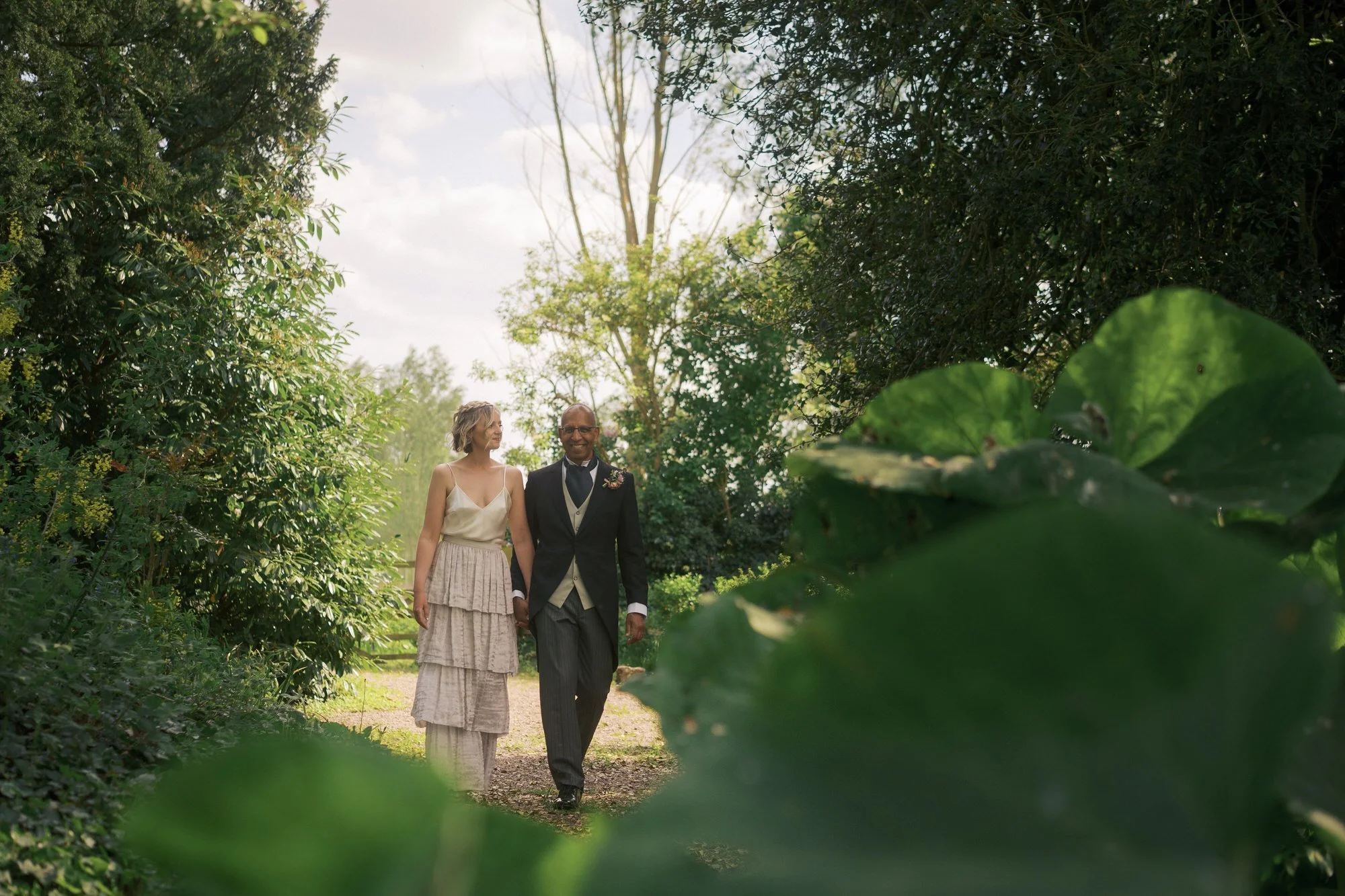 A couple walking along a garden path, seen through large green leaves