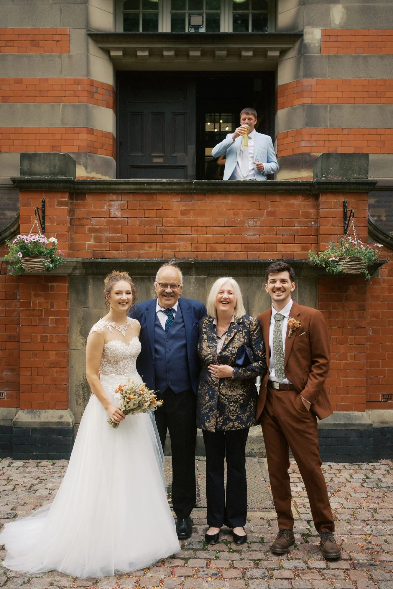 A family group in front of the entrance steps while a guest raises a pint from the doorway above, The Pumping House, Ollerton