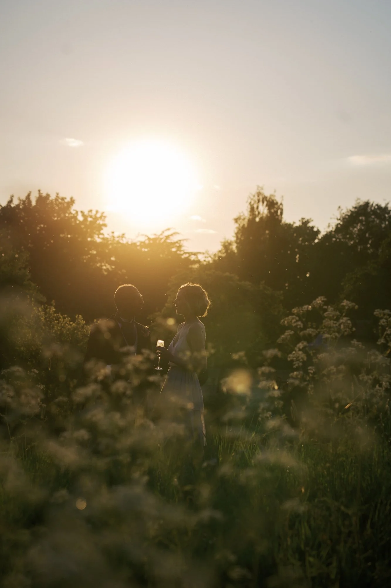 A couple silhouetted against the setting sun in long grass near the terrace at Hodsock Priory
