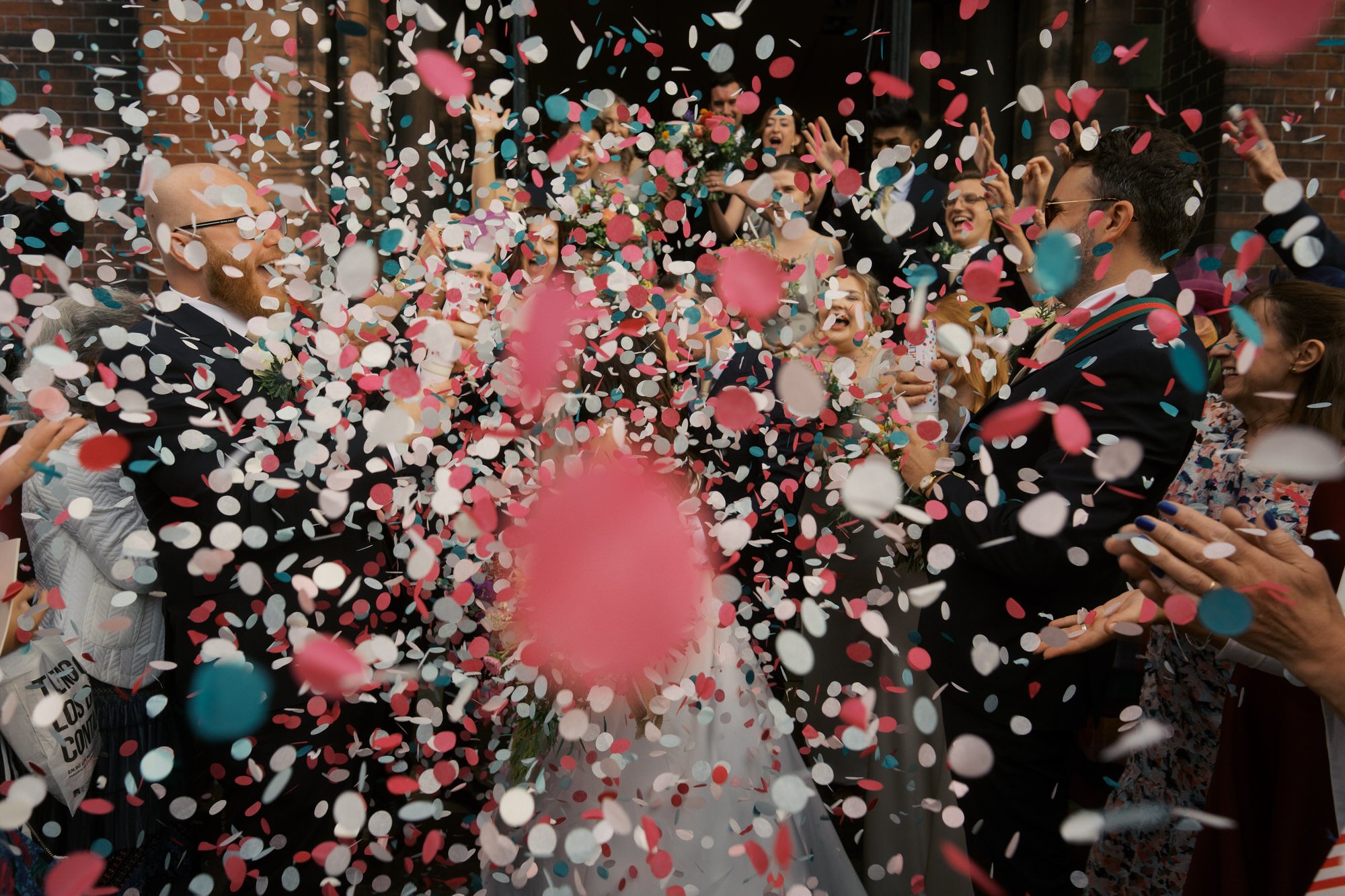 Bride and groom almost hidden in a cloud of pink, white and blue confetti thrown by cheering guests outside St Aidan's Church in Harehills.