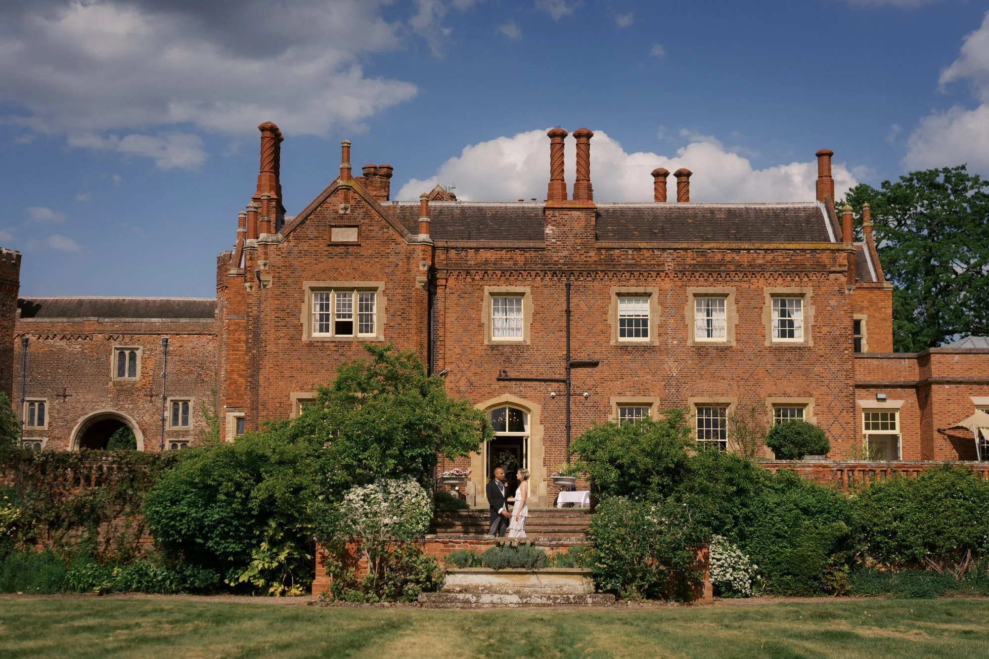 The red-brick front of Hodsock Priory under a blue sky with white clouds, Nottinghamshire