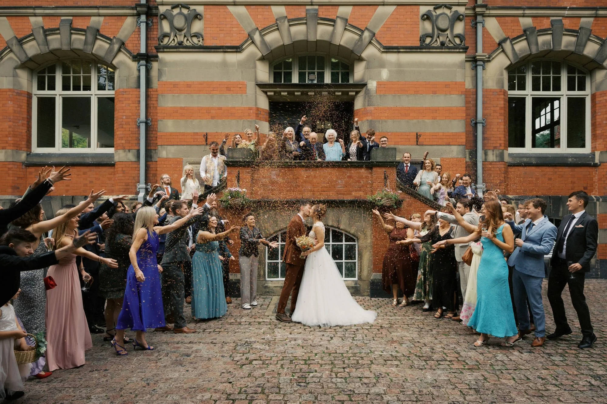 Guests throwing confetti over a bride and groom kissing on the front steps of The Pumping House, Ollerton