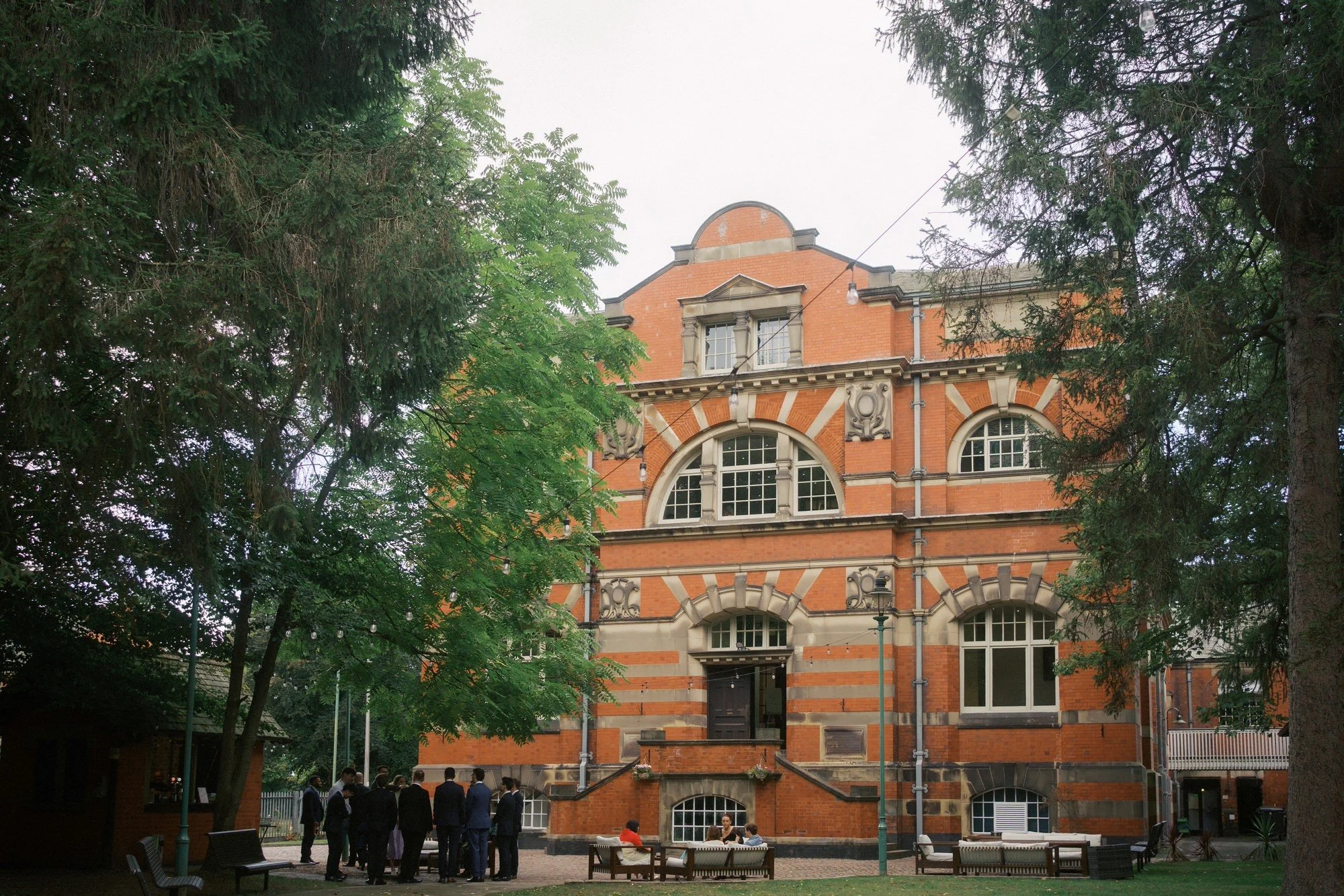 The red-brick Pumping House between tall trees, with guests gathered by the outdoor bar, Ollerton, Nottinghamshire