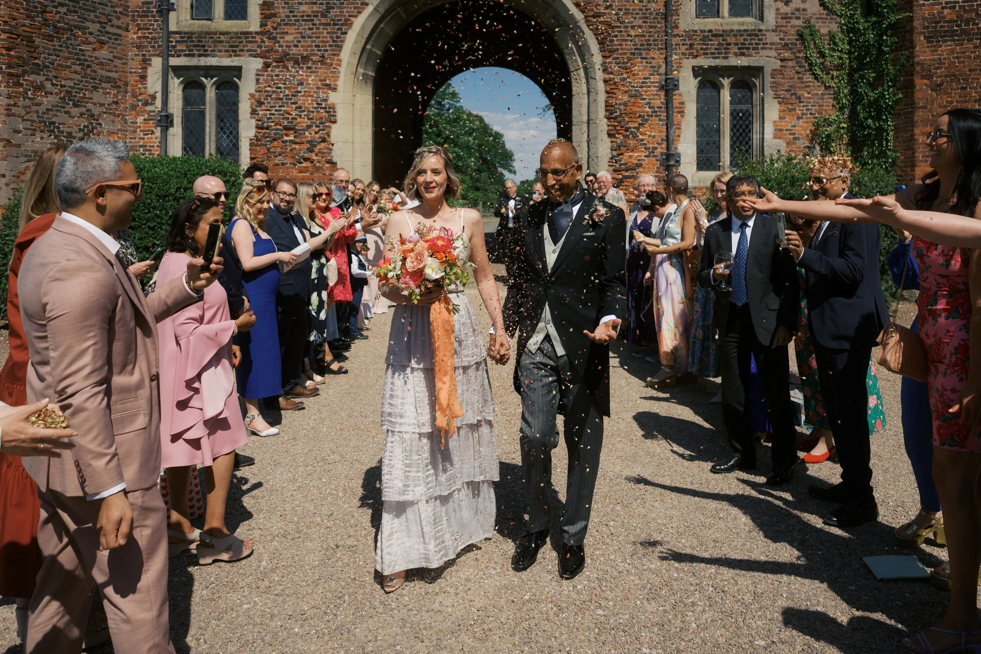 A couple walking through a shower of confetti under the brick Gatehouse arch at Hodsock Priory