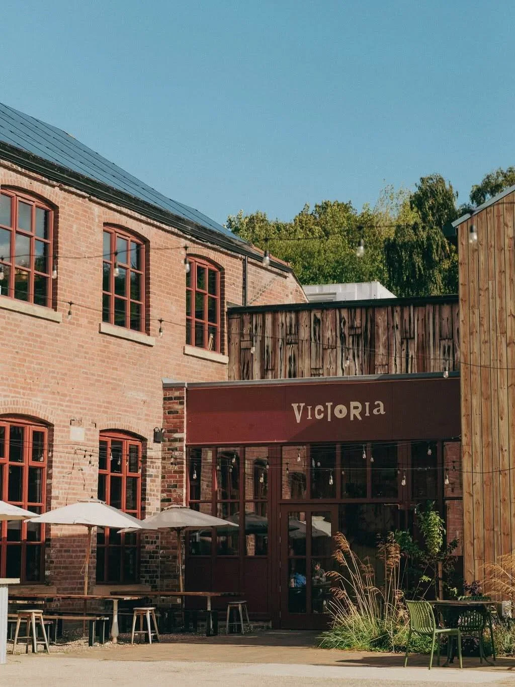 Exterior of The Victoria in Neepsend, Sheffield, with red-framed arched windows, the entrance under the venue's sign and outdoor seating in the courtyard