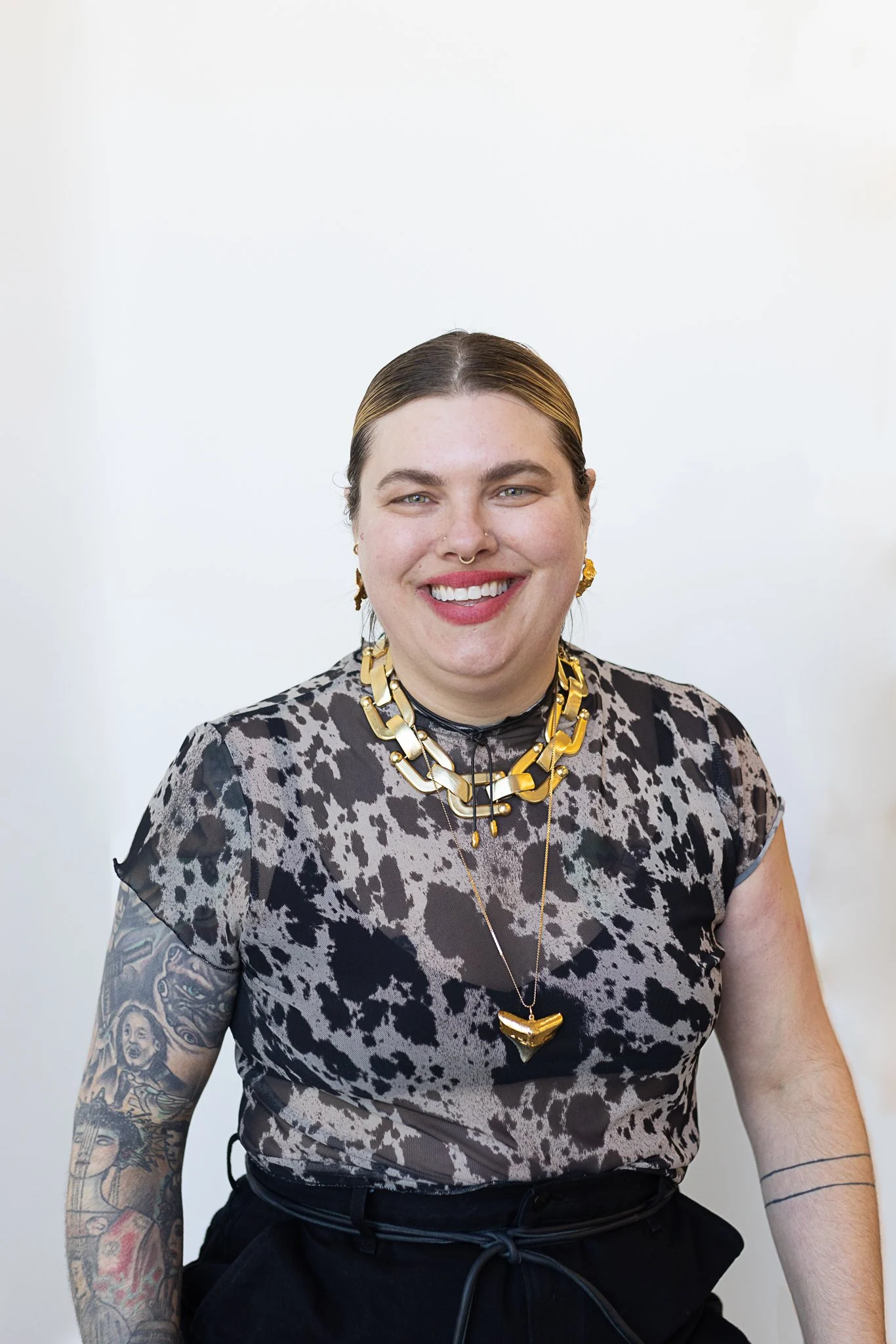 A stylist with pulled-back brown hair wearing a patterned shirt and bold gold jewelry