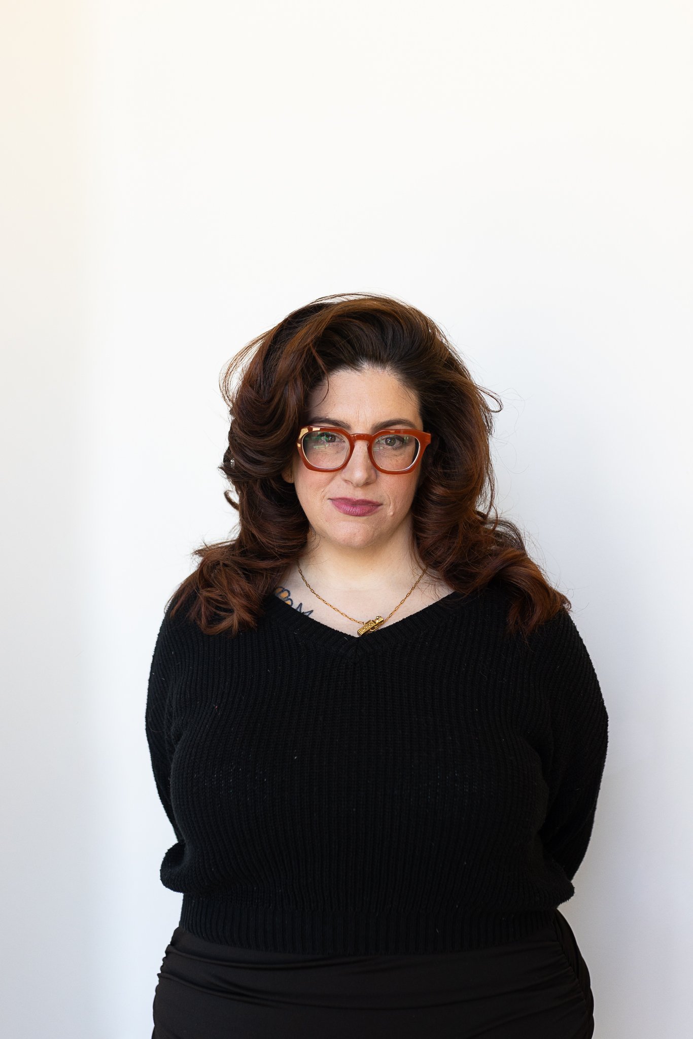 A stylist with long, wavy, reddish brown hair wearing glasses and a black top