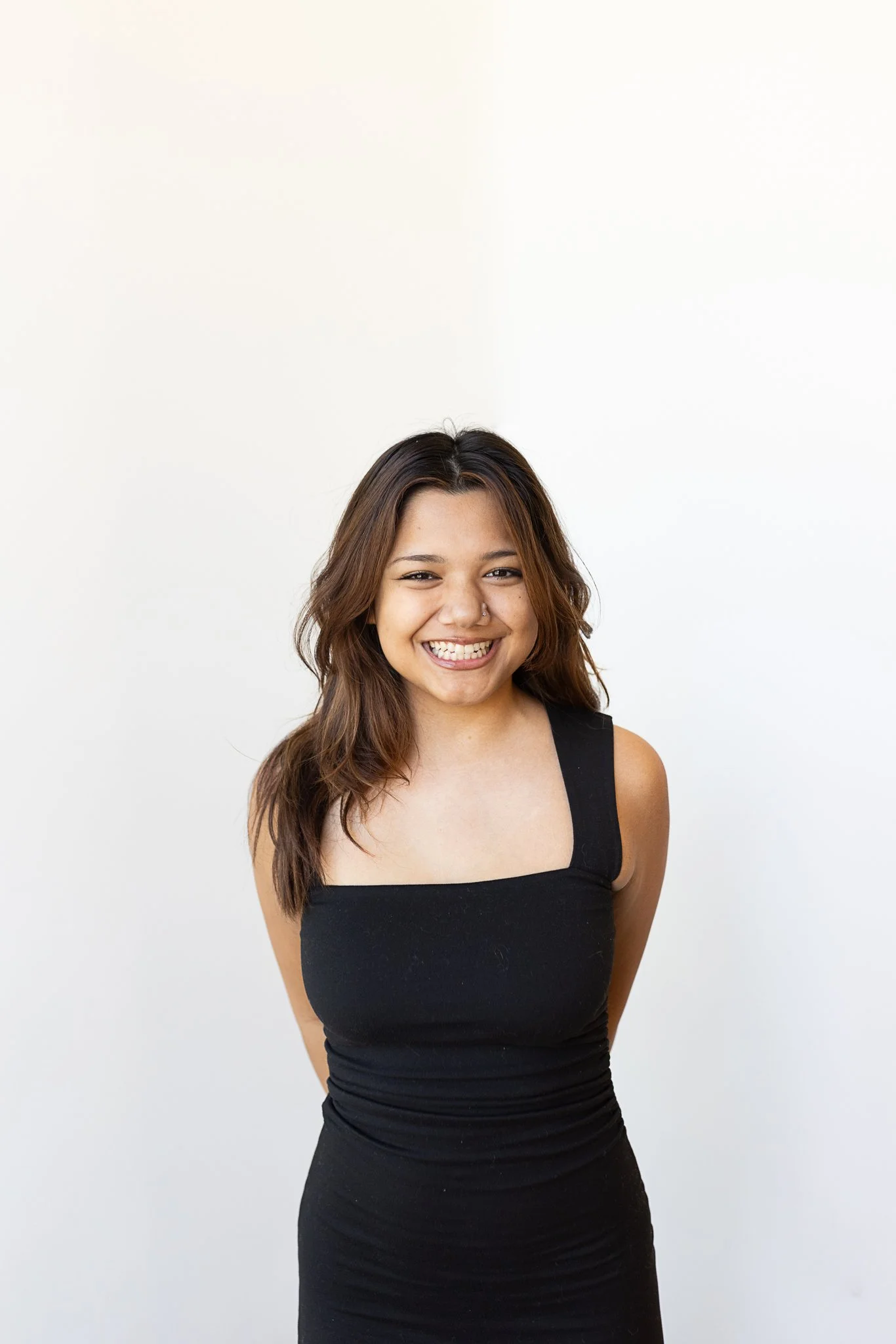 A stylist with long, layered, and wavy brown hair wearing a black dress