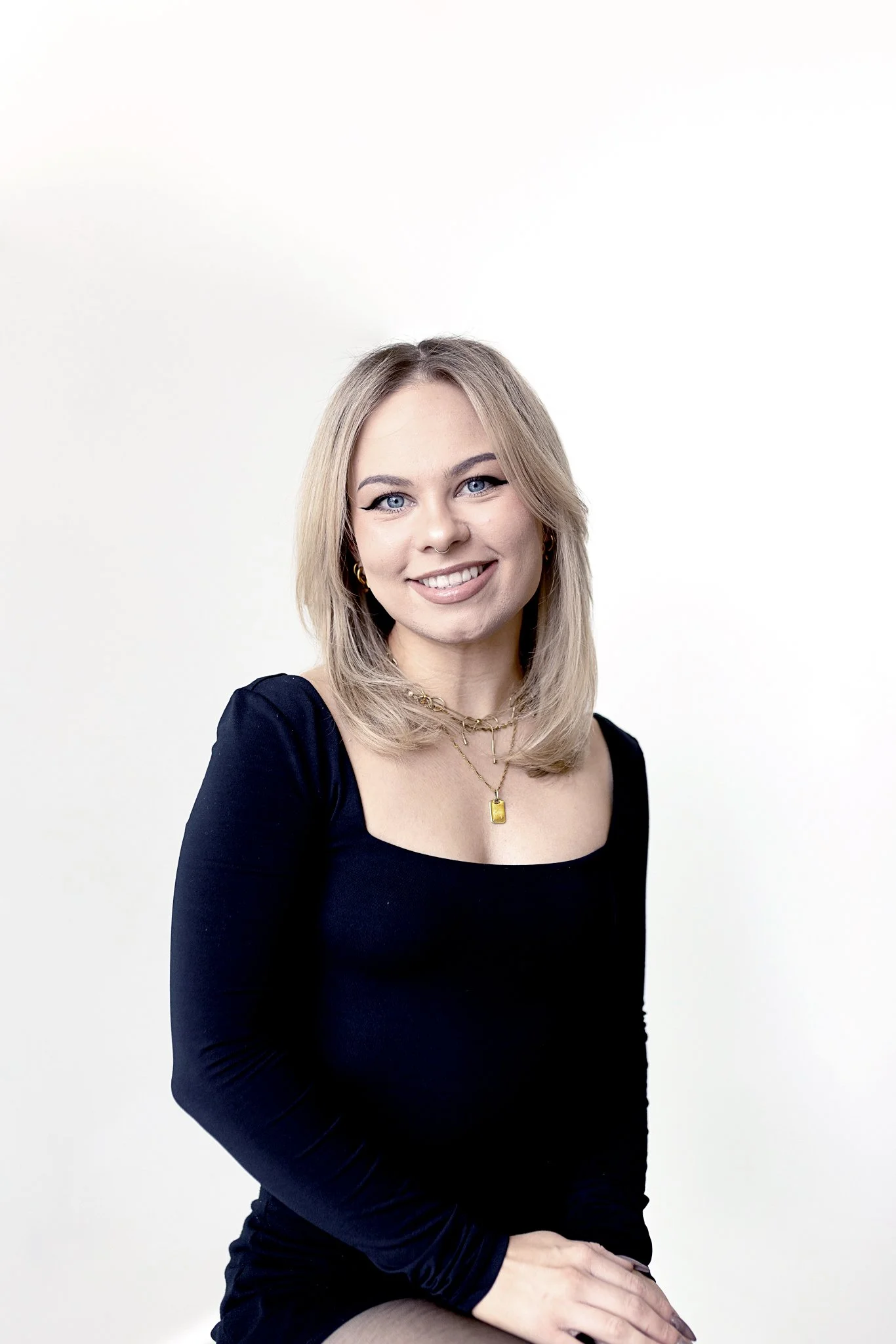 A stylist with shoulder-length and layered straight blonde hair, wearing a black top