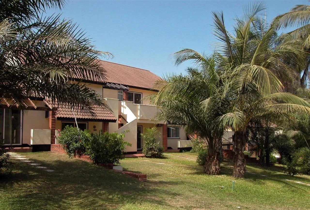 A residential complex with palm trees and lush green grass under a clear blue sky.