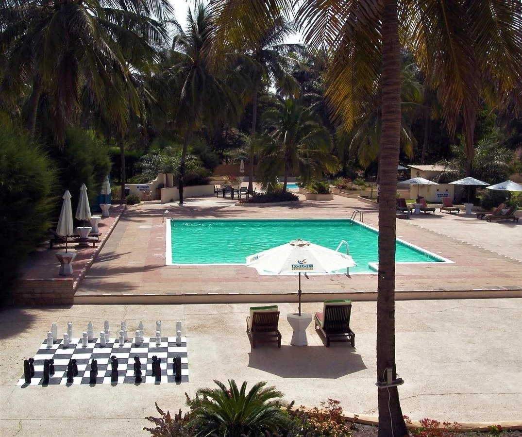 Swimming pool surrounded by lounge chairs and umbrellas, with tall palm trees and lush greenery in the background.