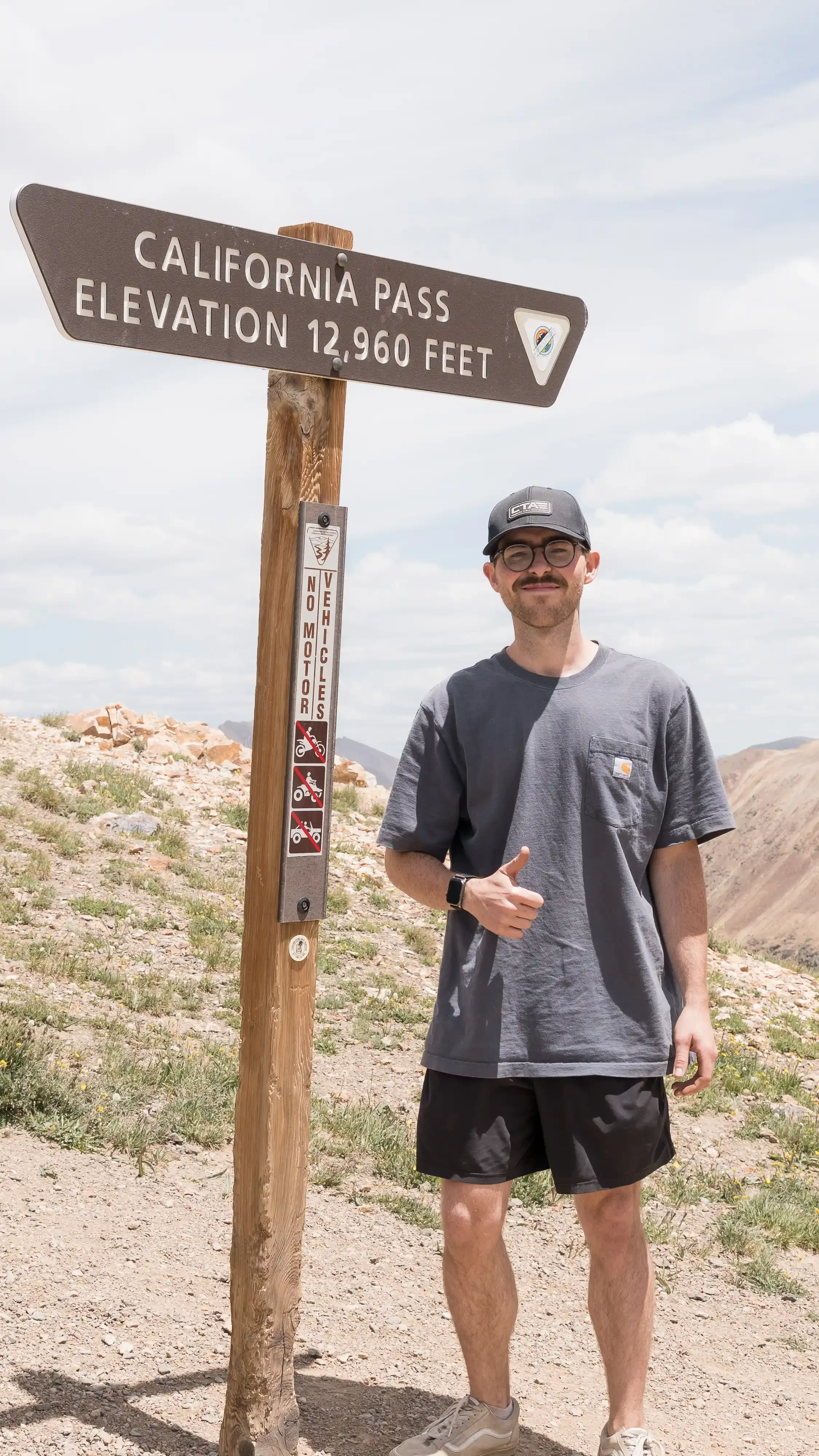 Jordan Weaver, founder of Overlandaholic, standing in front of California Pass Elevation 12,960 Feet sign in Colorado.