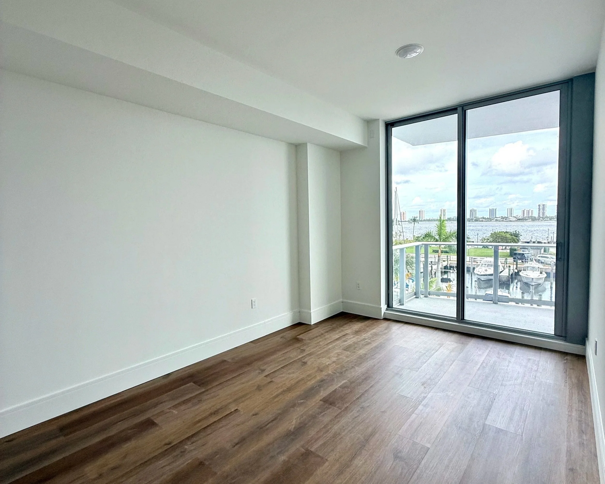 Empty narrow bedroom in a new-construction condo with a sliding door to a balcony overlooking the marina