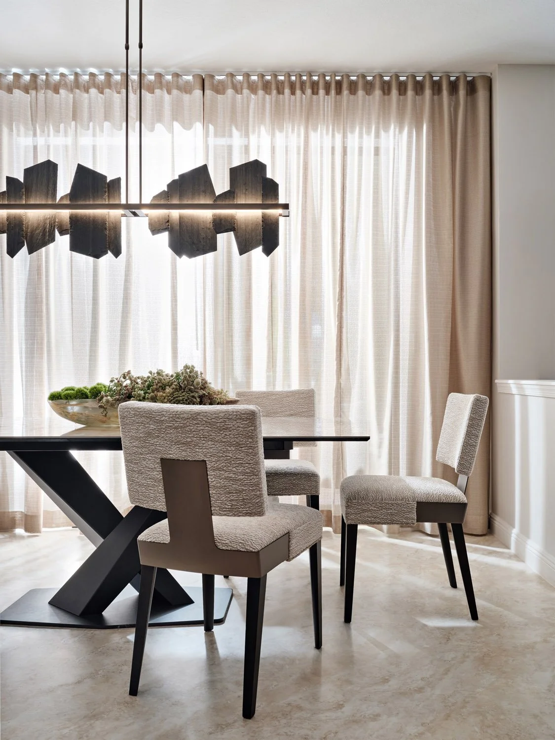 Contemporary dining area with statement light fixture, sheer curtains, and chairs.jpg