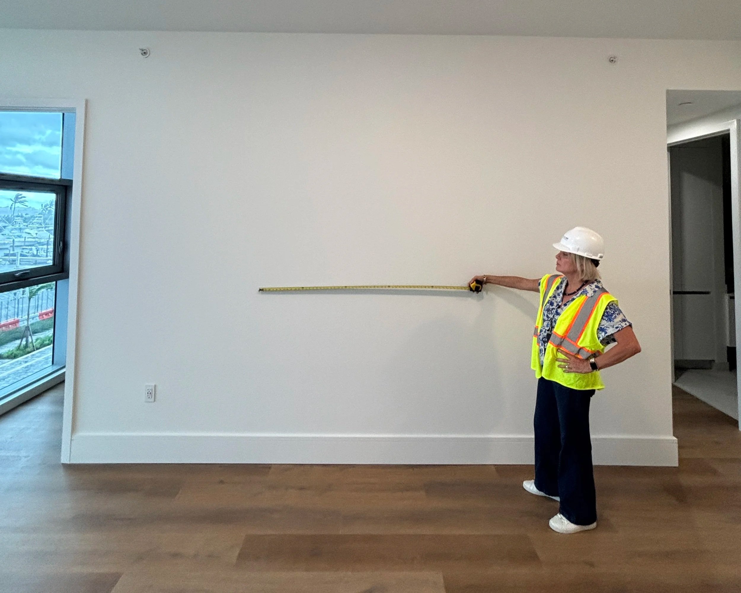 Interior designer Maritza Capiro measuring a blank wall in an empty new-construction waterfront condo