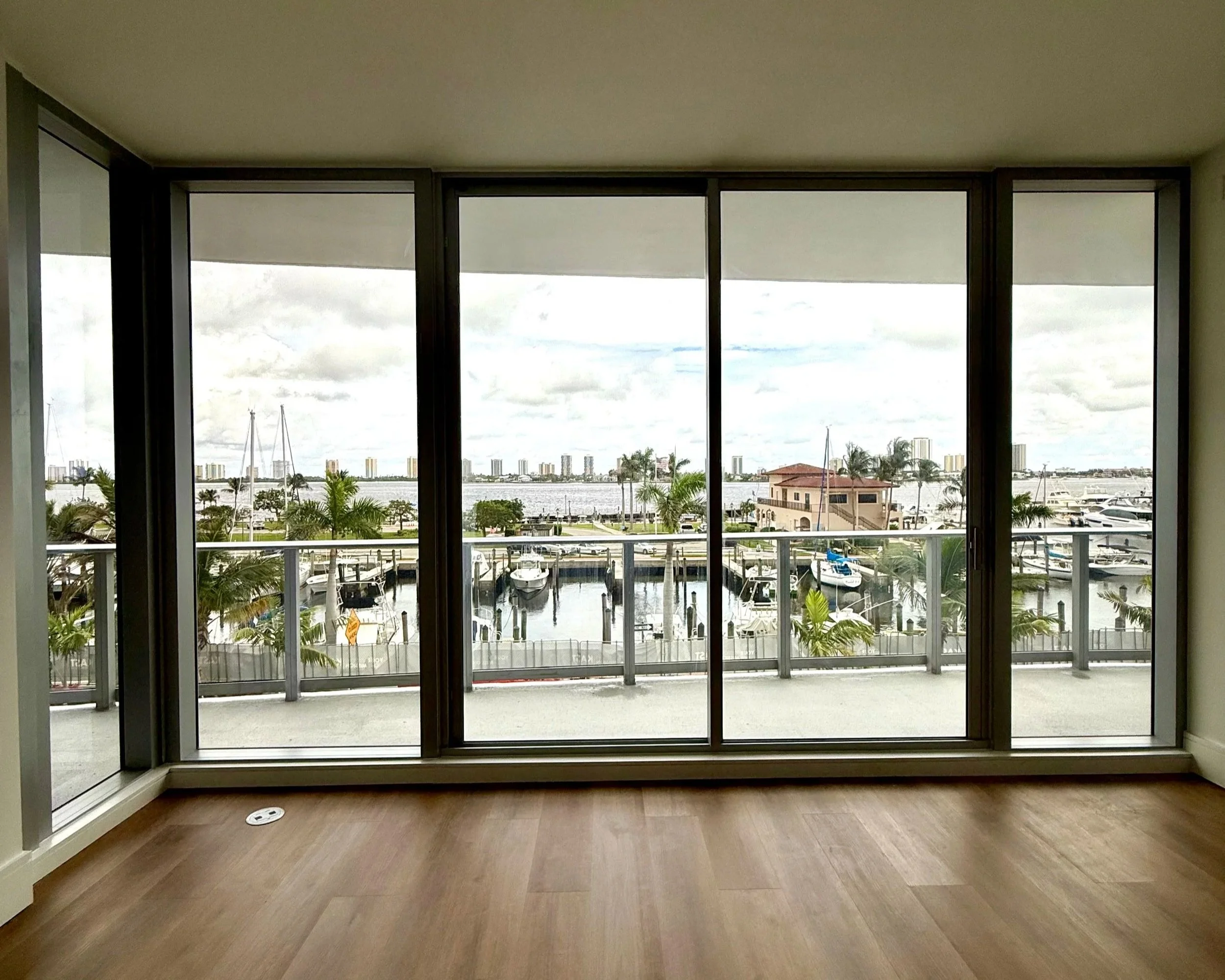 Empty living room of a new-construction waterfront condo with floor-to-ceiling windows overlooking a marina