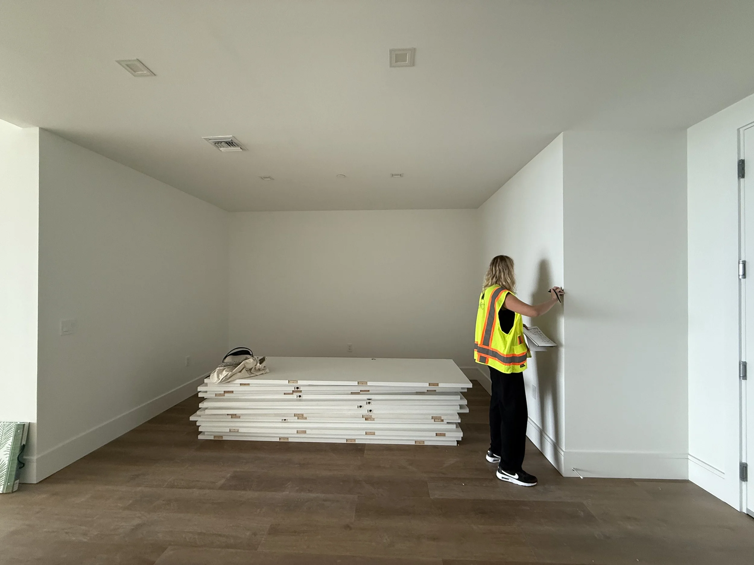Empty room in a new-construction condo before the custom home office, with millwork panels stacked on the floor and the wall being marked for installation