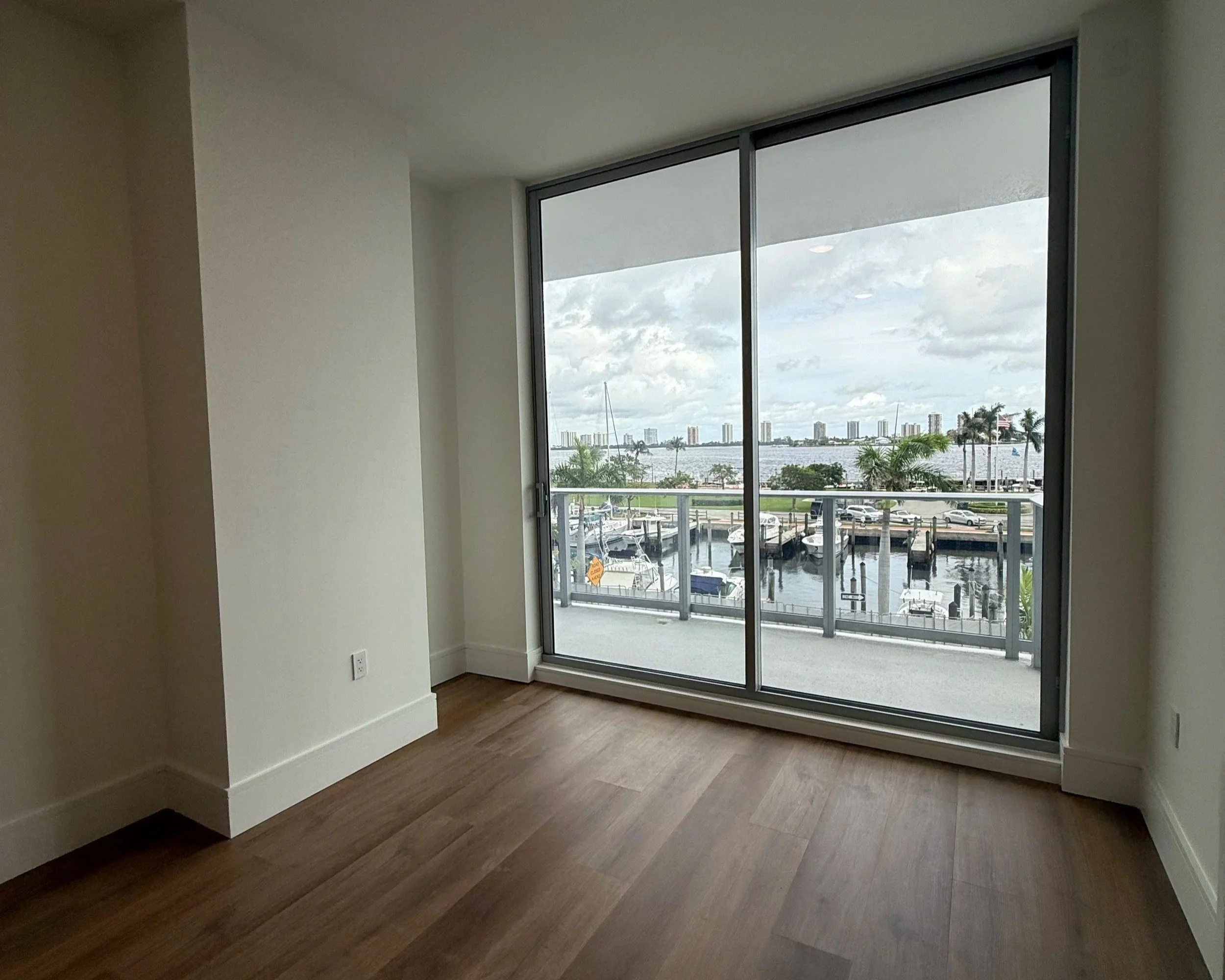 Empty primary bedroom in a new-construction waterfront condo with a sliding glass door to a balcony overlooking the marina