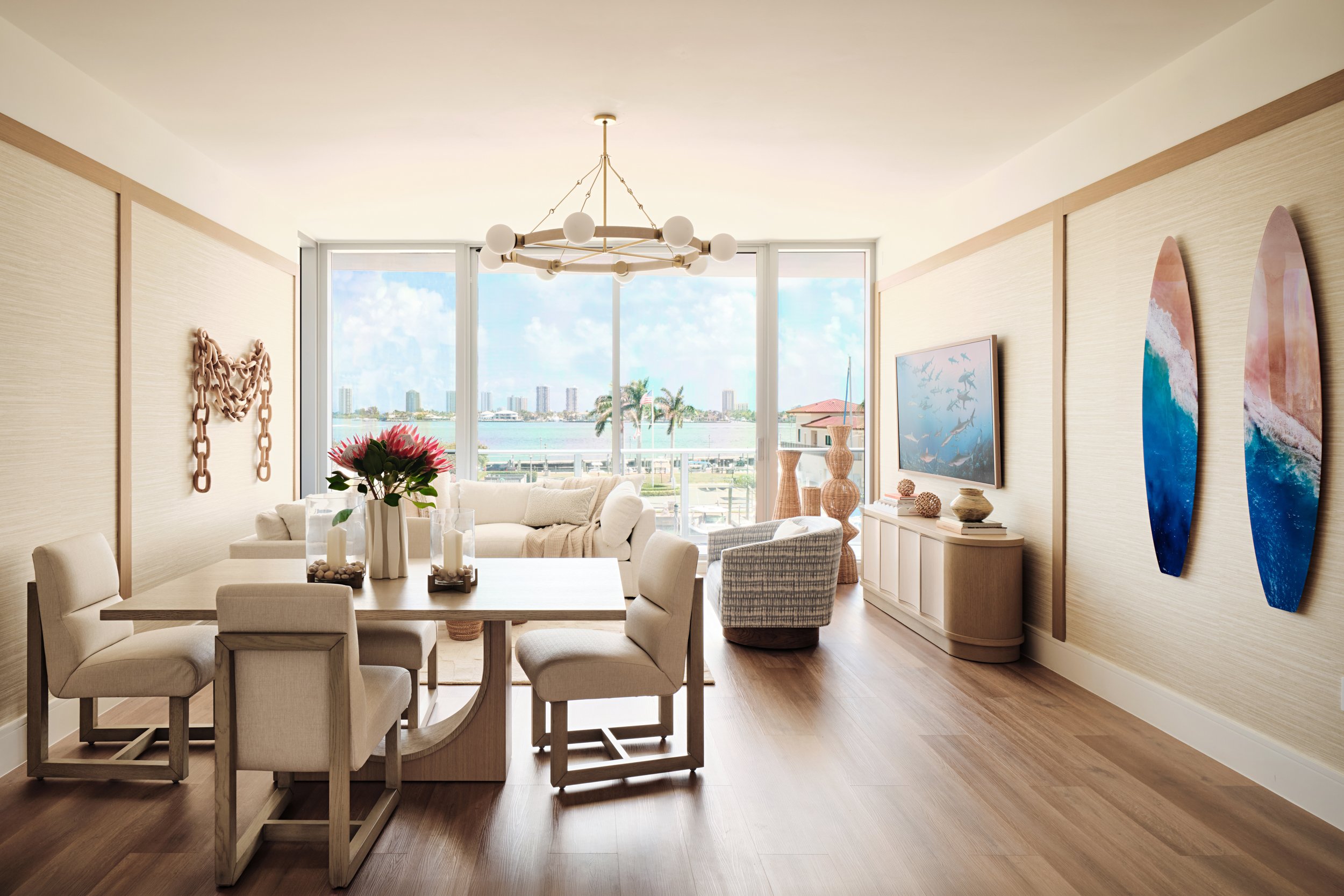 Living and dining room in a waterfront condo with a globe ring chandelier, sculpted wood dining table and water views