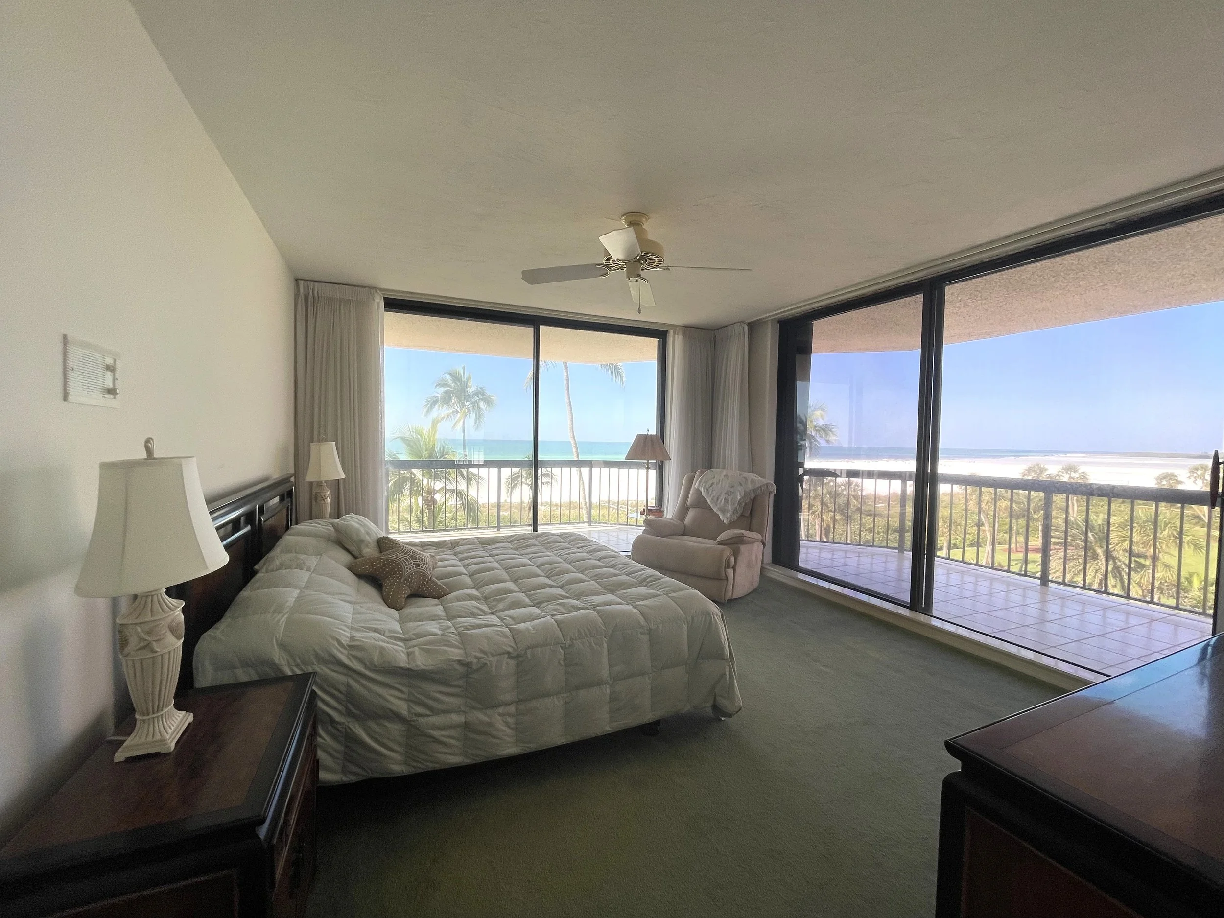 Primary bedroom at The Duchess on Marco Island before renovation, with dark wood furniture, green carpet and wraparound Gulf views