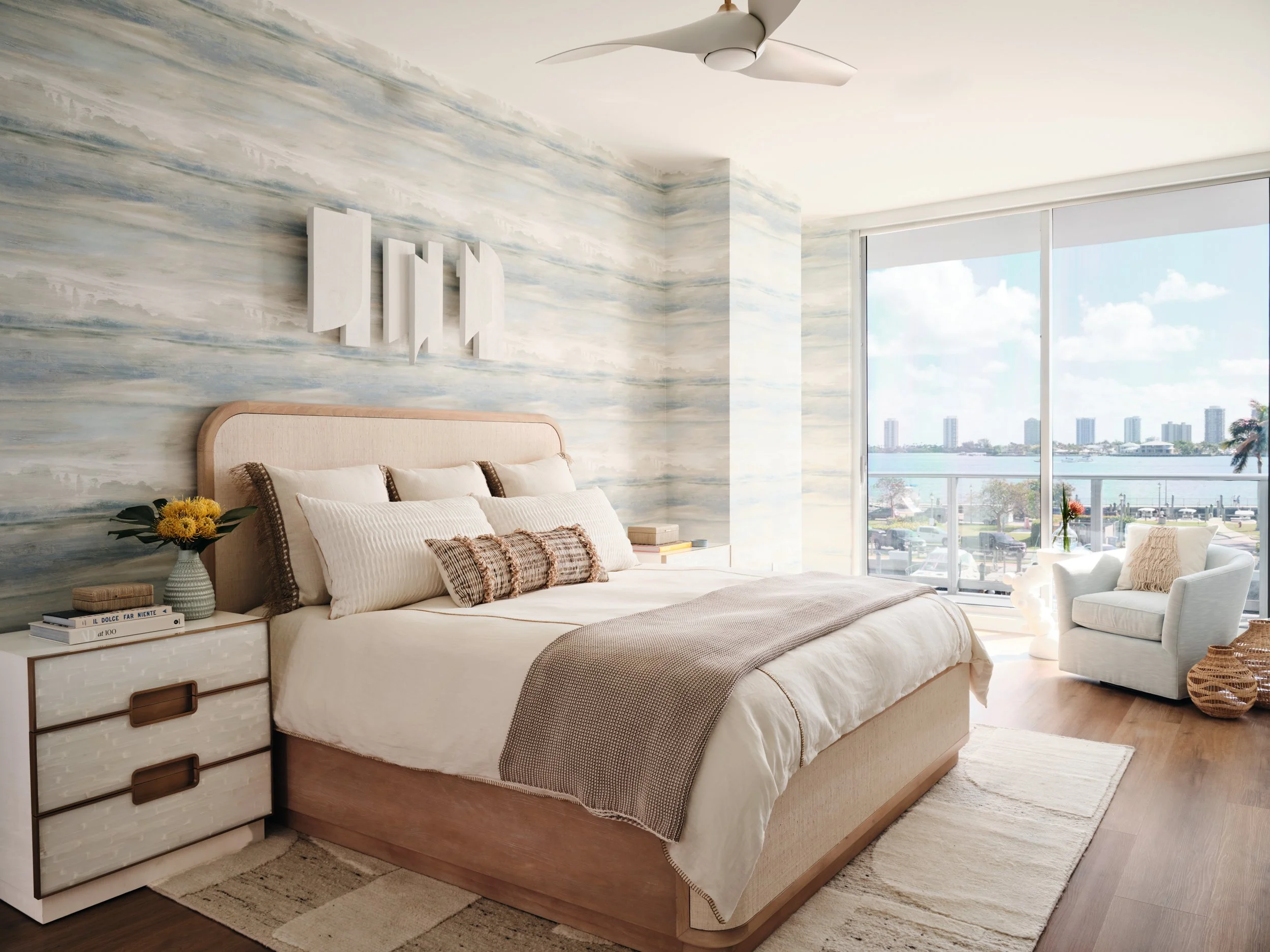 Primary bedroom with blue watercolor wallcovering, a raffia-wrapped bed and water views