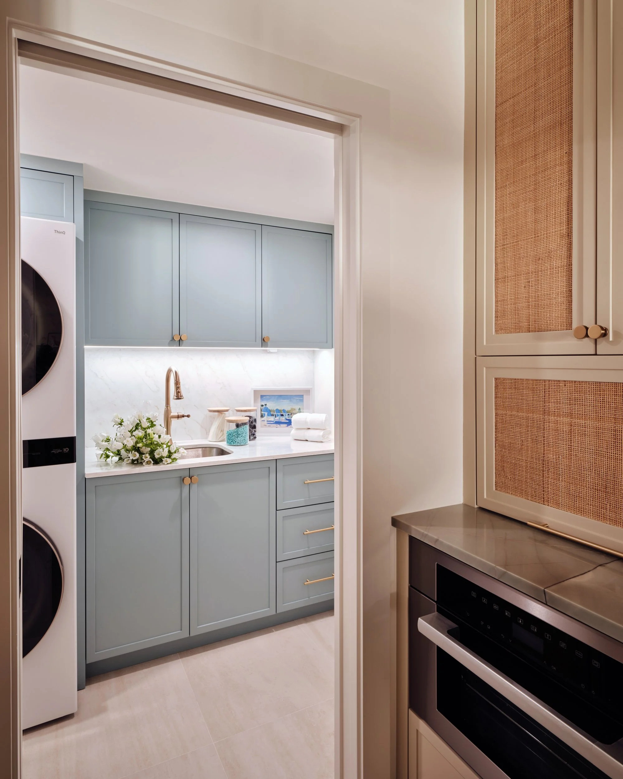 Laundry room at The Duchess on Marco Island with slate blue cabinetry, a stacked washer and dryer and brass hardware, seen from the kitchen