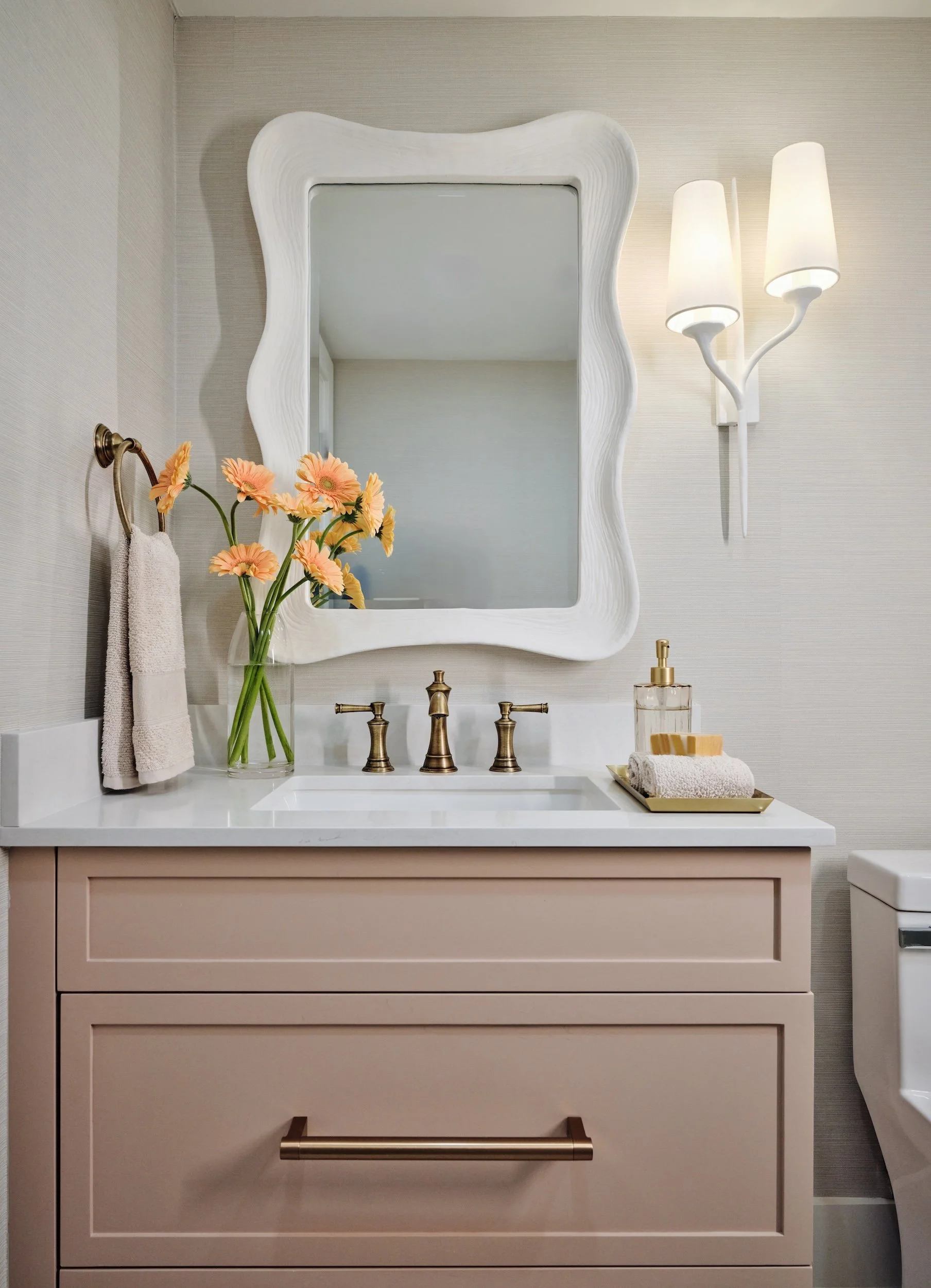 Guest bath at The Duchess on Marco Island with a blush vanity, sculptural white mirror and brass faucet