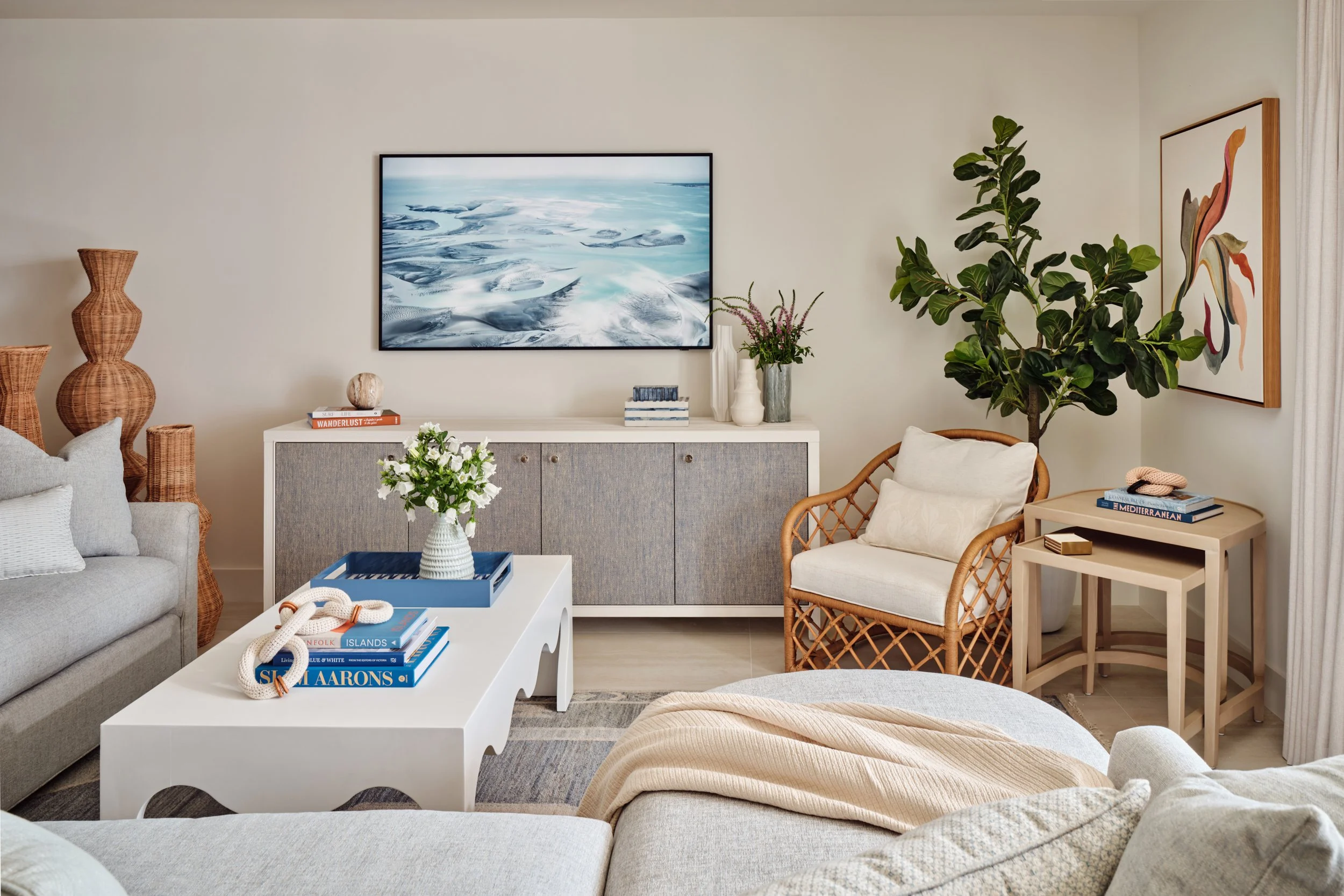 Living room at The Duchess on Marco Island with a sectional, white scalloped coffee table, media console and rattan armchair