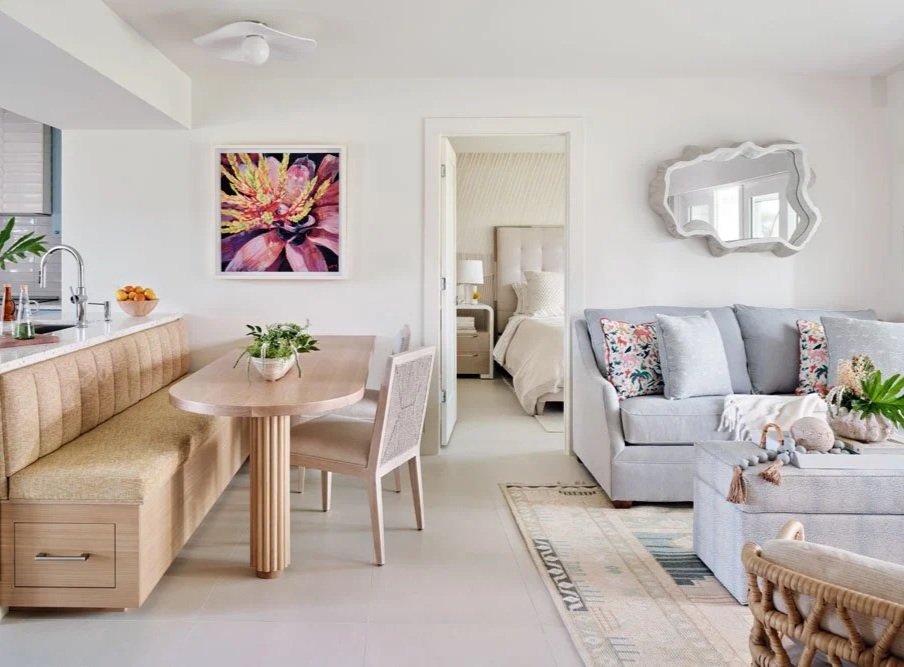 Living room with beige built-in bench seating, a wooden dining table, and a light-colored upholstered chair. Bright, airy pops of color elevate this South Florida home.