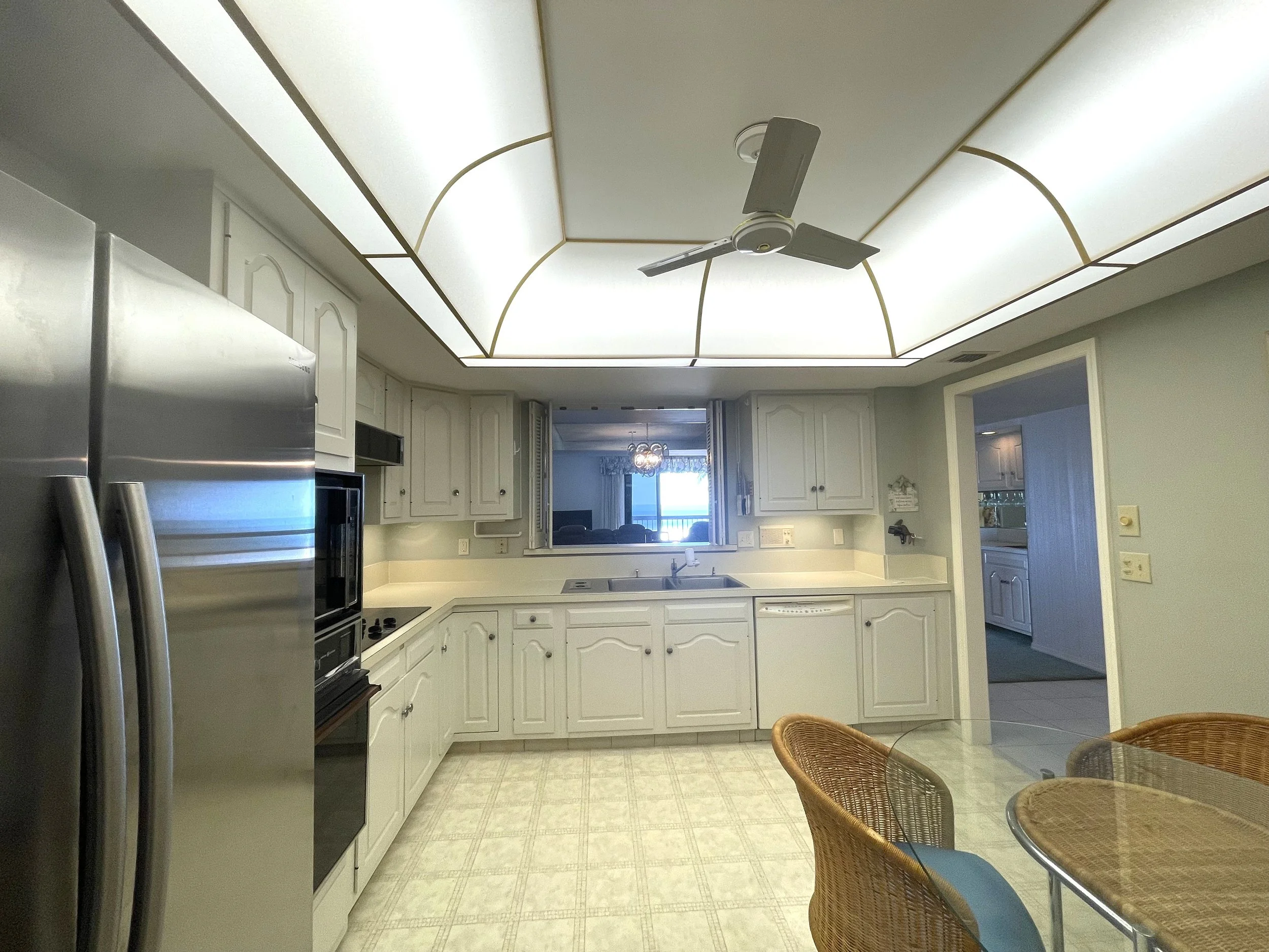 Kitchen at The Duchess condo on Marco Island before renovation, with white cabinets, a lit dropped ceiling and a pass-through window