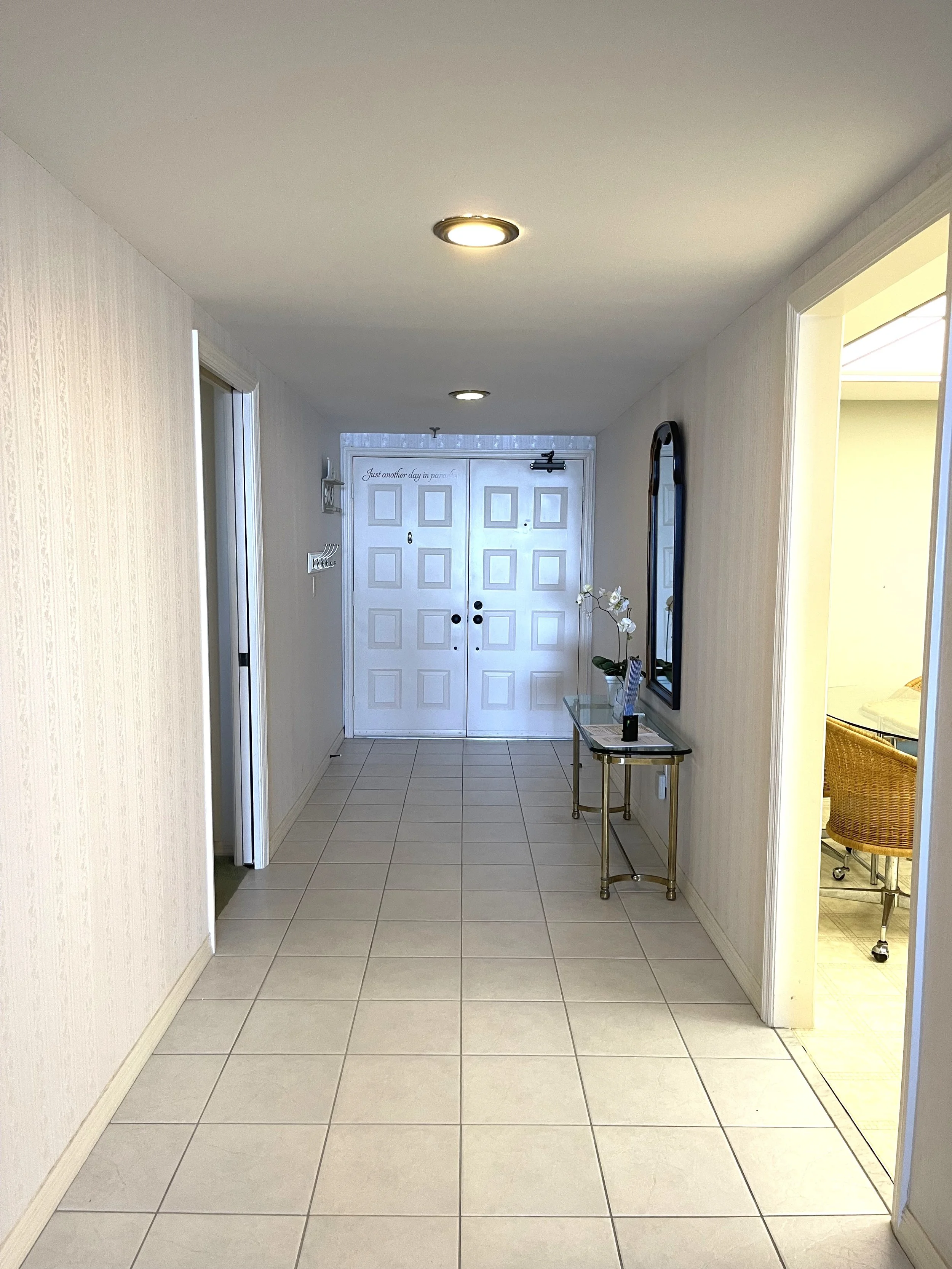Entry hallway at The Duchess condo on Marco Island before renovation, with patterned wallpaper, beige tile and a glass console