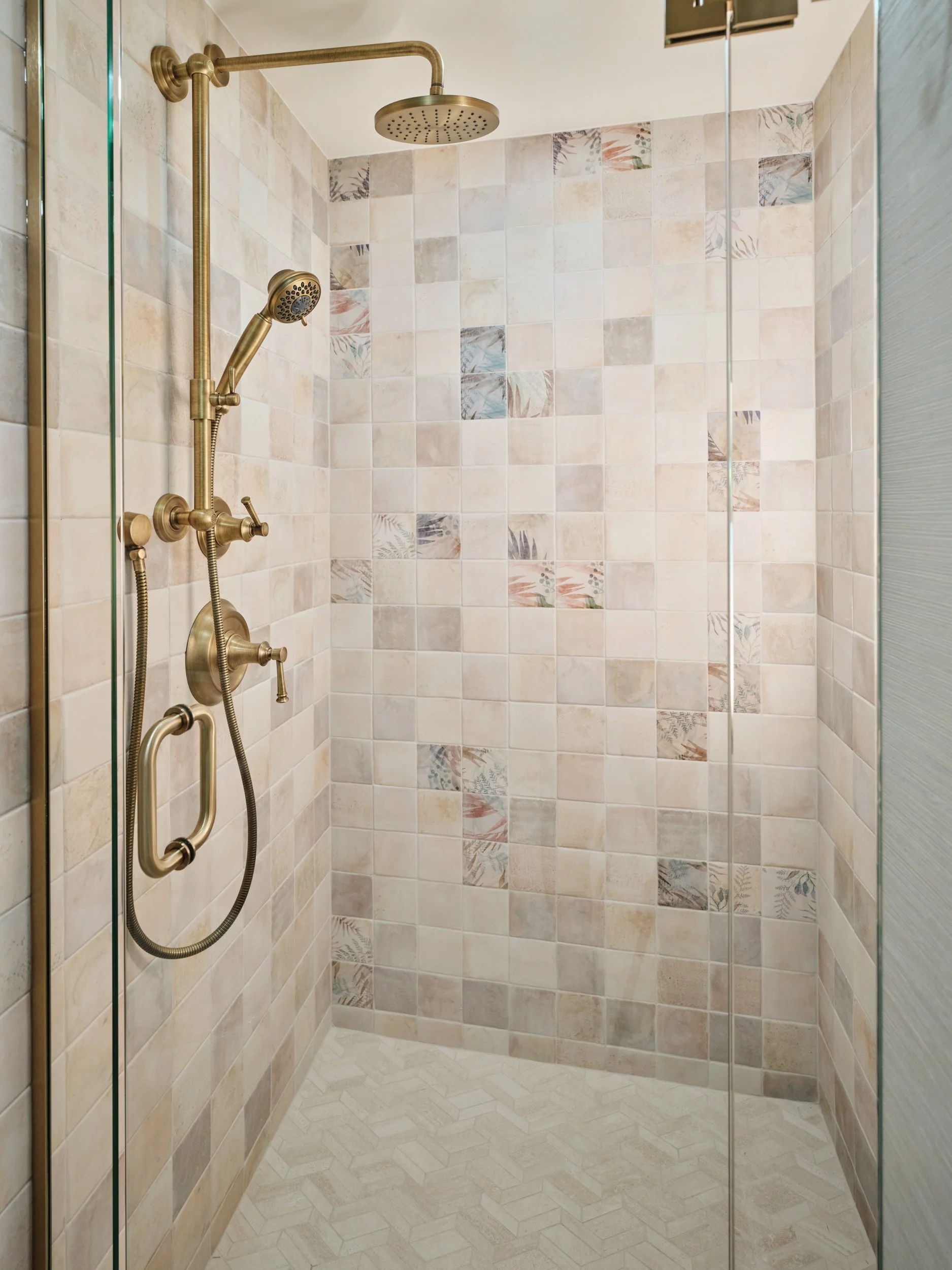 Walk-in shower in a Marco Island condo guest bath with handmade-look tile, botanical accent tiles and brass fixtures