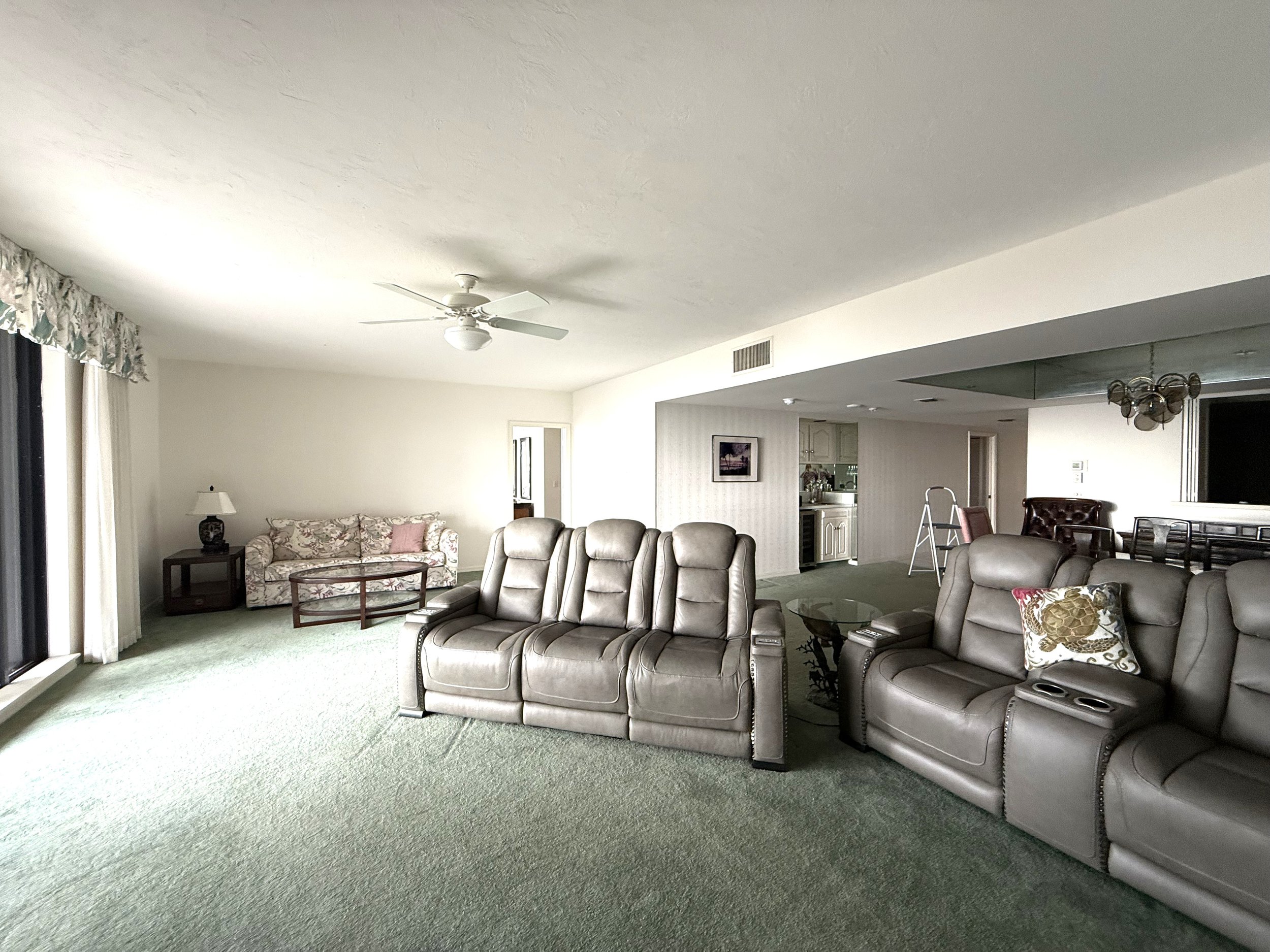Living room at The Duchess condo on Marco Island before renovation, with green carpet, leather recliners and a dated wet bar