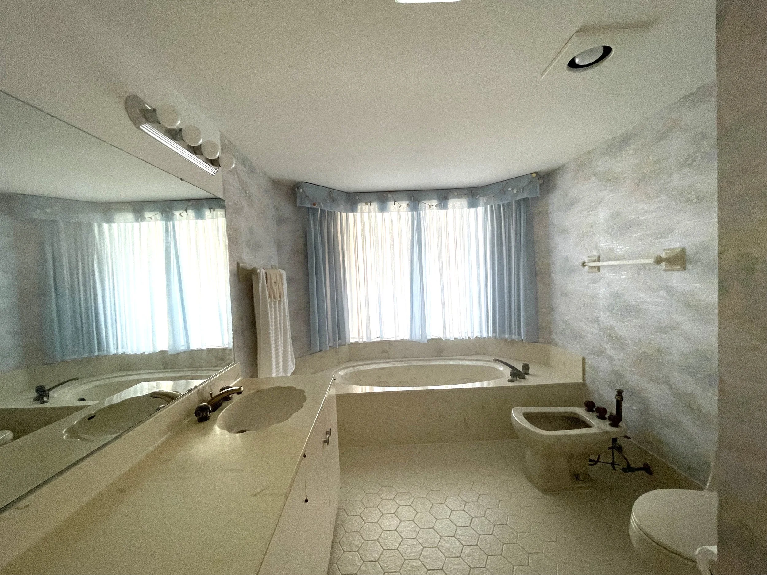 Primary bathroom at The Duchess condo on Marco Island before renovation, with a platform tub, curtained windows and a bidet