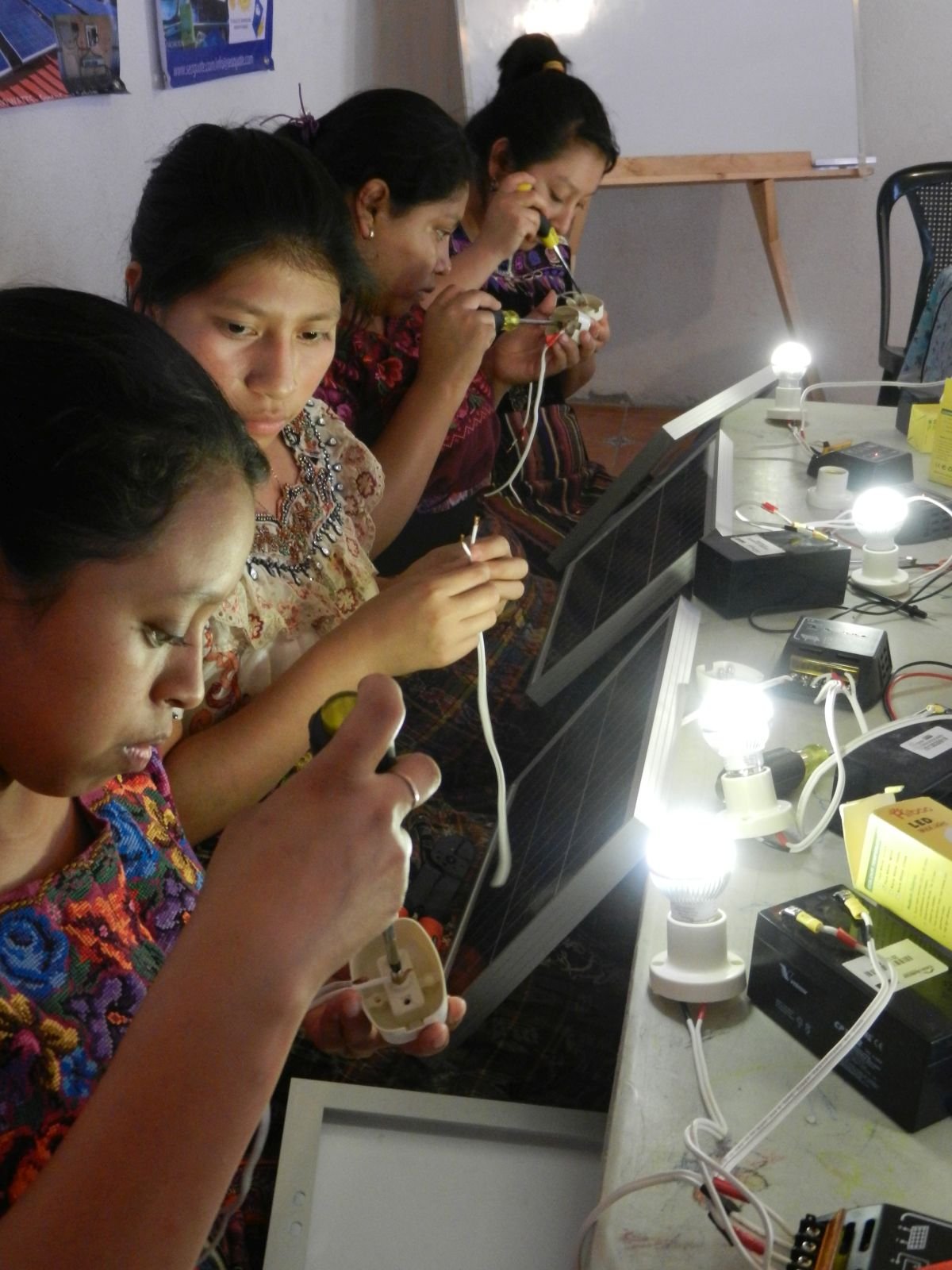 Women working on electronic devices at a workshop with small light bulbs, circuit boards, and laptops on the table.