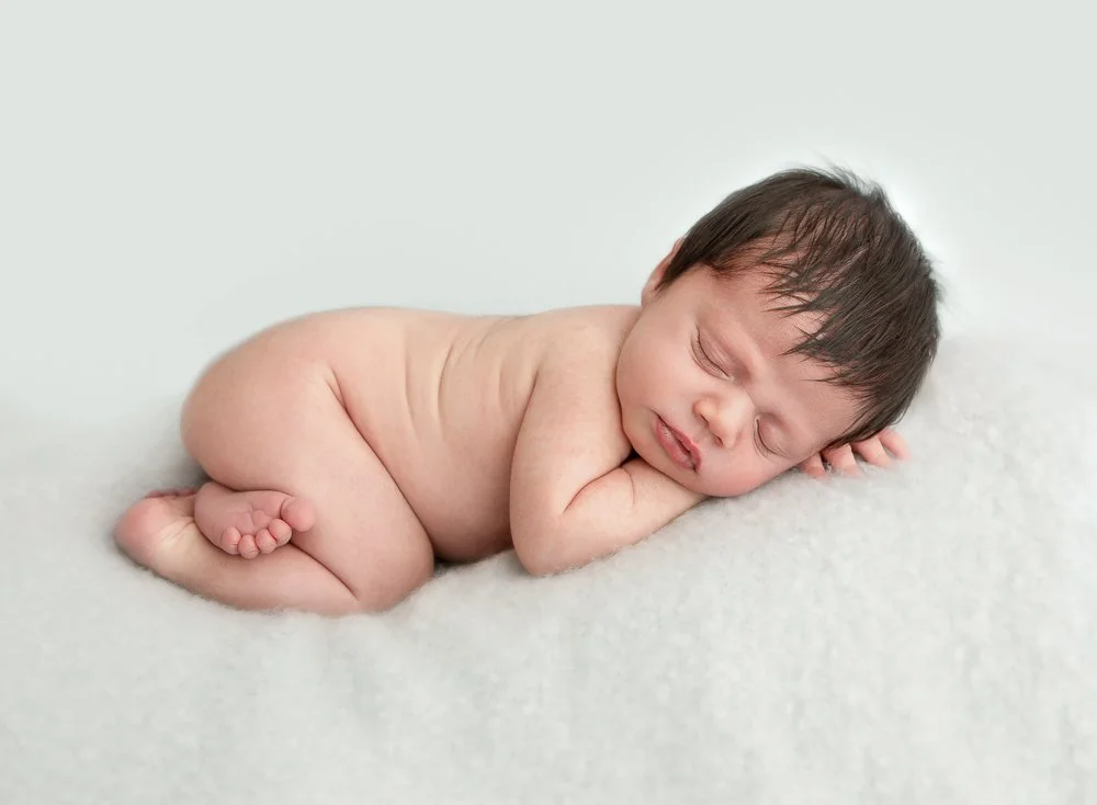 A peacefully sleeping baby lying on a soft surface with arms tucked under its head and eyes closed.