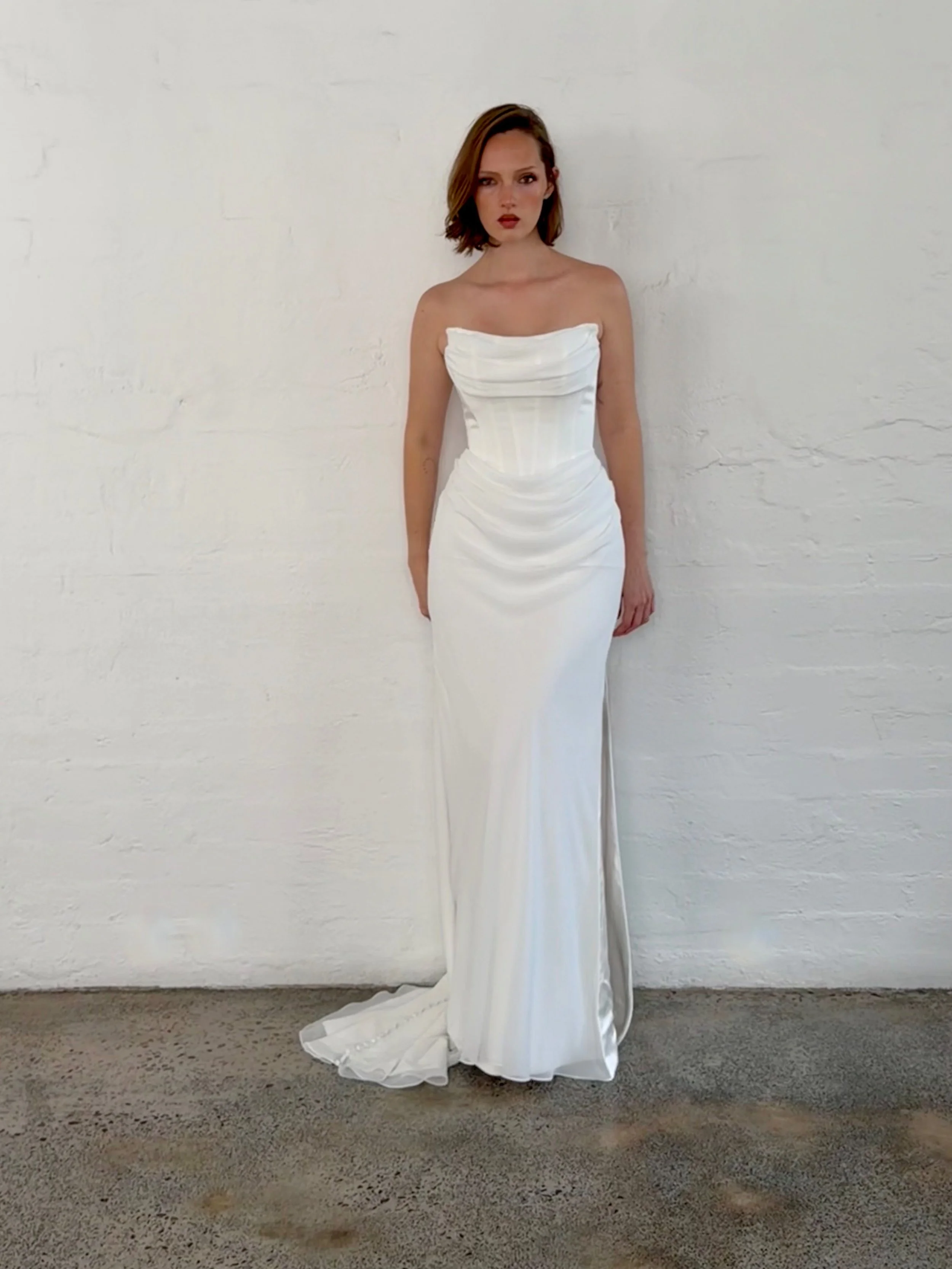 A study in understated elegance, Eloise II is designed for the modern bride who appreciates timeless sophistication. Crafted from luxurious chiffon, this strapless gown features a softly draped neckline and a structured corset bodice that beautifully