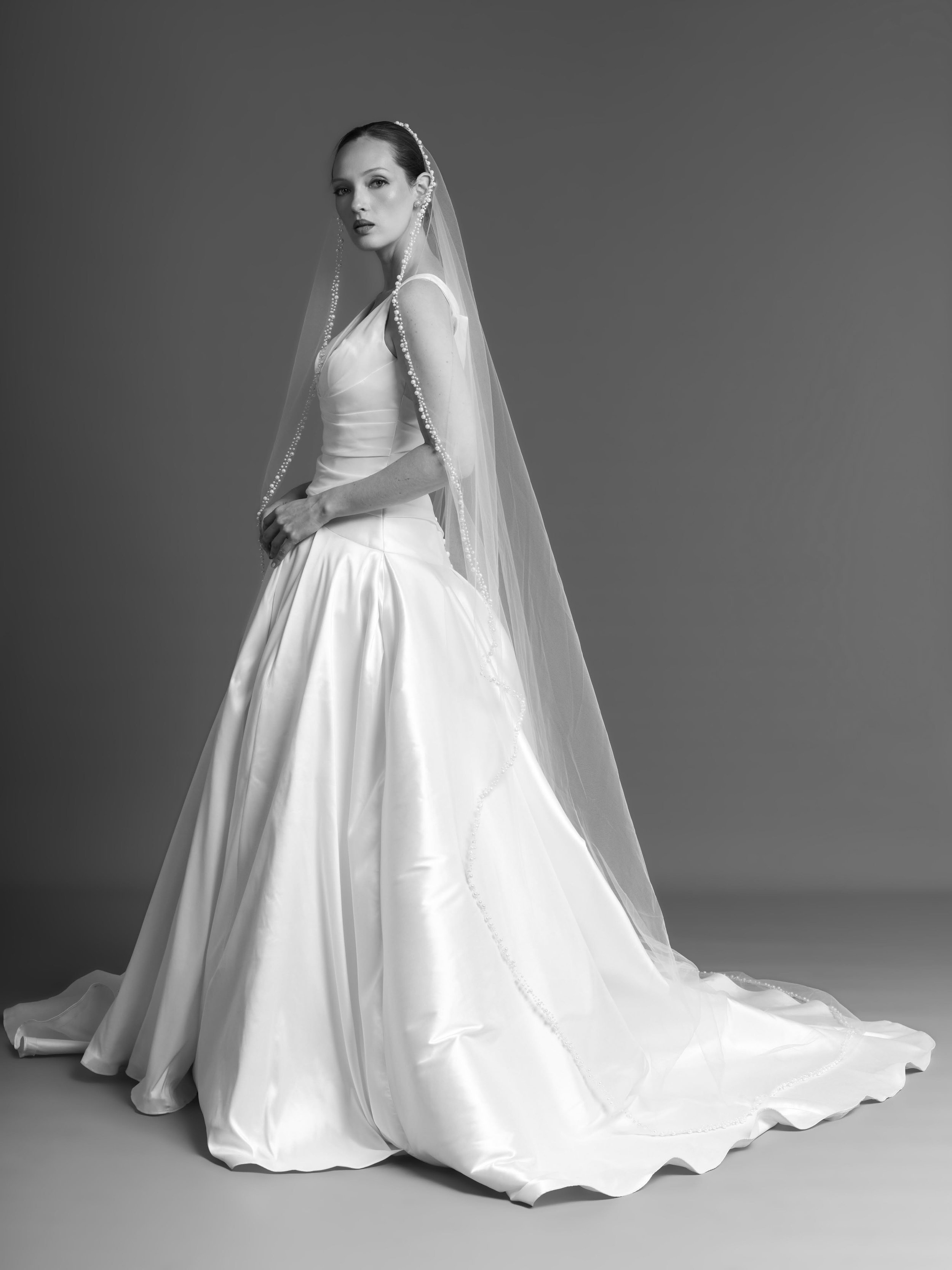 Modern Romance, Reimagined. There is something undeniably cinematic about Evie. The silhouette feels unapologetically grand, yet the restraint of its clean lines gives it an unmistakably modern attitude.
Fluid folds catch the light. A voluminous trai