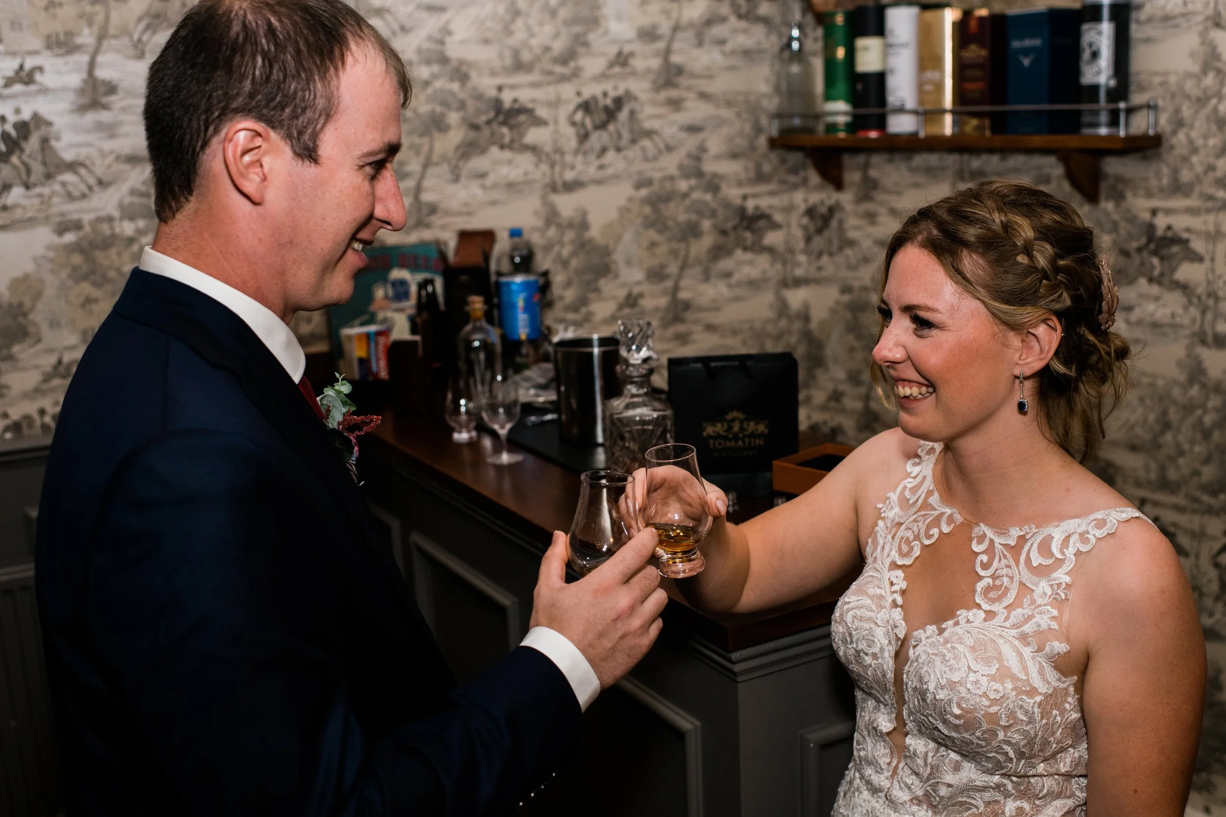 A bride and groom smiling and giving a toast at their wedding reception, with the bride in a lace wedding dress and the groom in a dark suit.