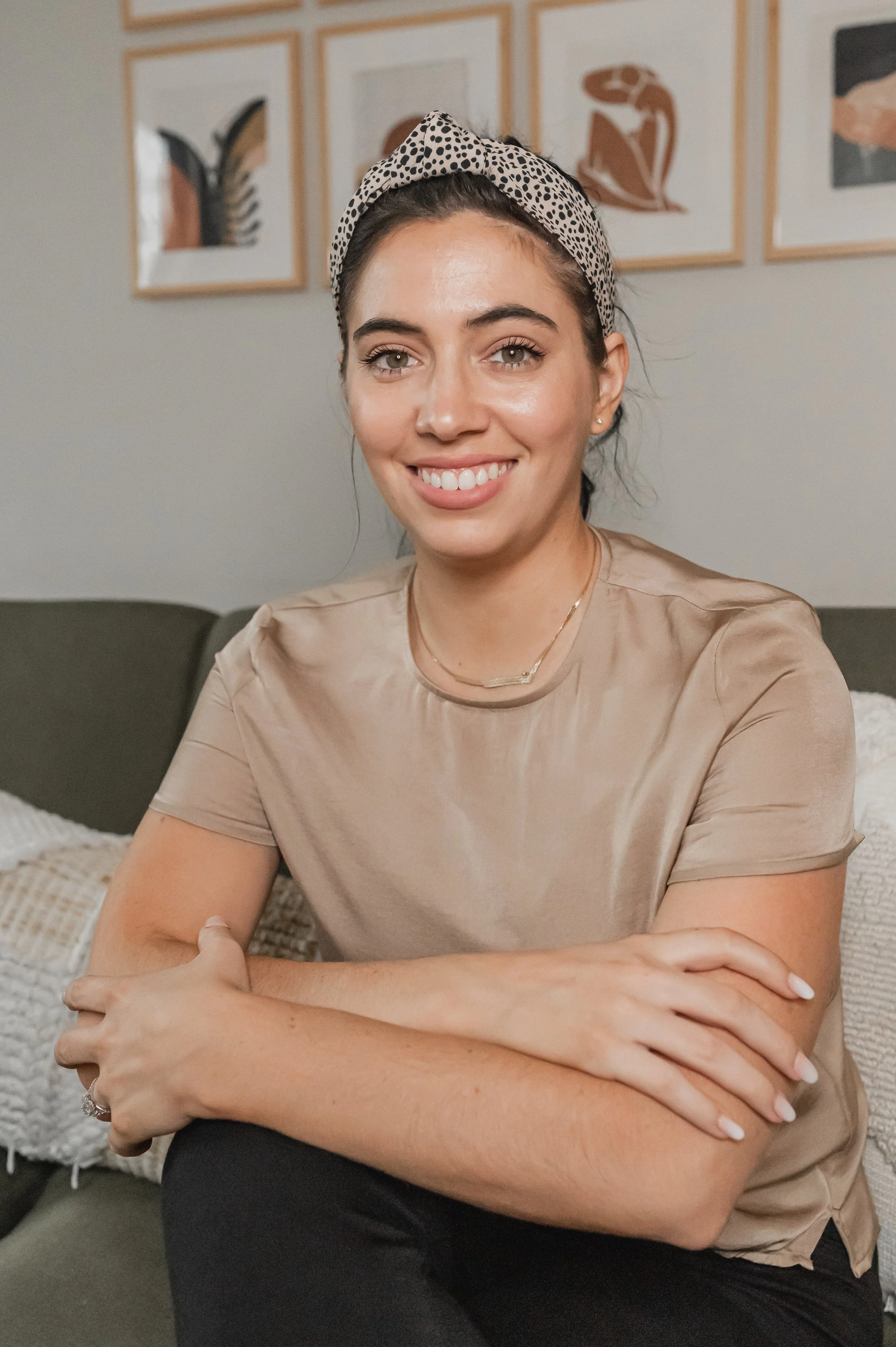 Image of Hannah Conner, a woman with brown hair wearing a spotted headband sitting with her arms crossed and resting on her knees wearing black pants and a brown short sleeve shirt, smiling warmly depicting an OCD therapist in Chicago